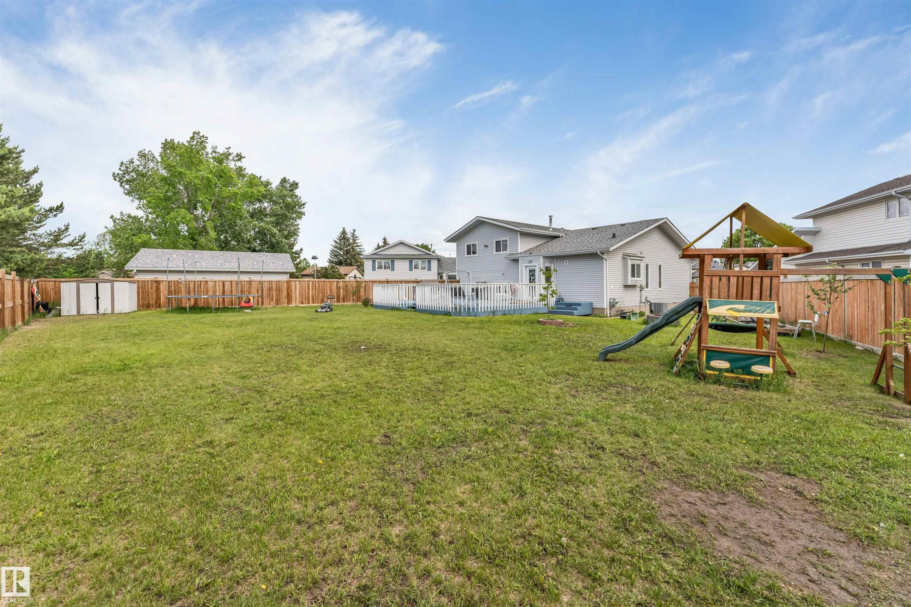 Expansive backyard featuring a manicured lawn, full wood fencing, and a multi-level deck off the residence - 3332 43 Street Nw, Edmonton, AB