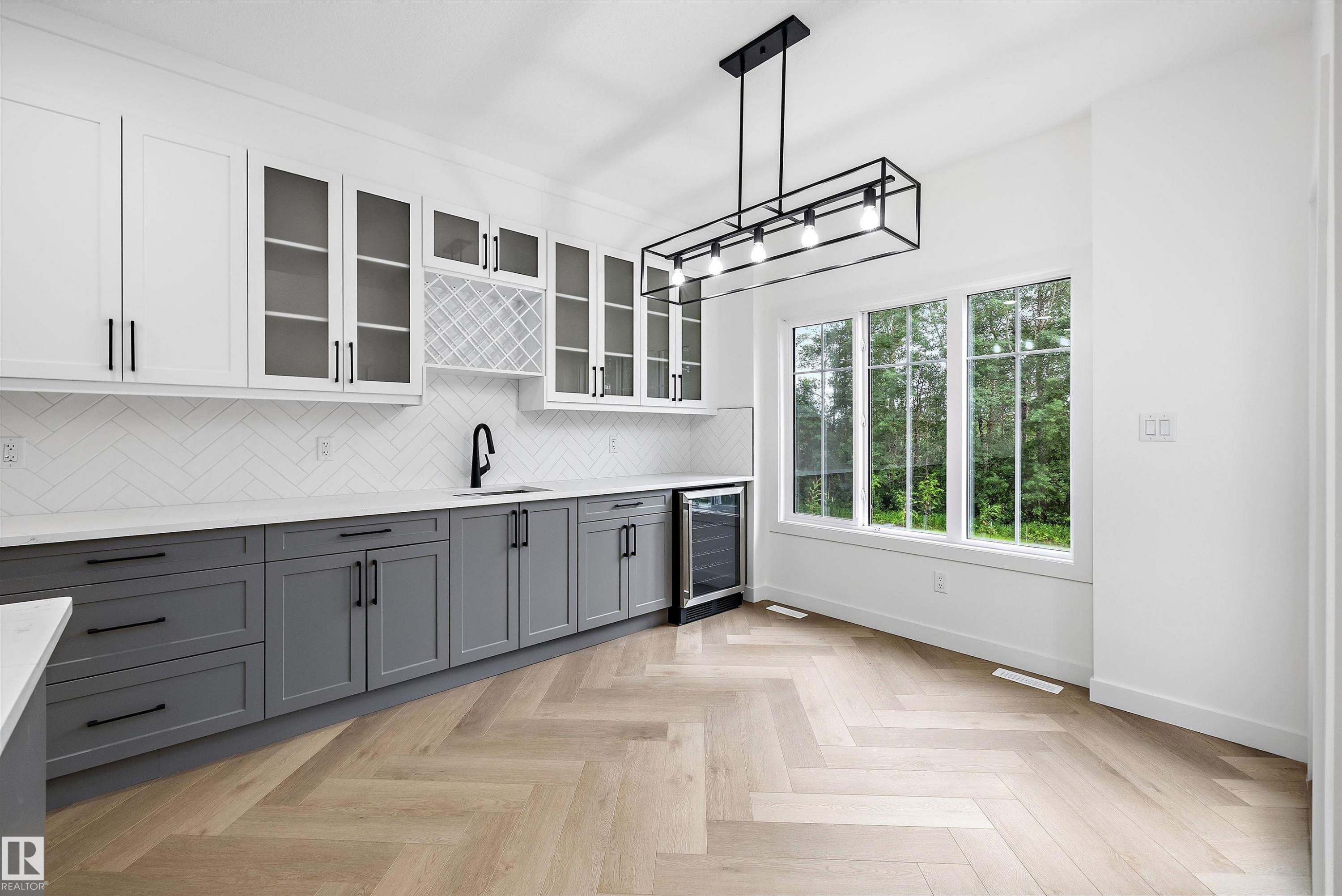 Kitchenette featuring two-tone cabinetry with black hardware, white herringbone tile backsplash, and a built-in beverage cooler - 917 Elderberry Landing, Edmonton, AB