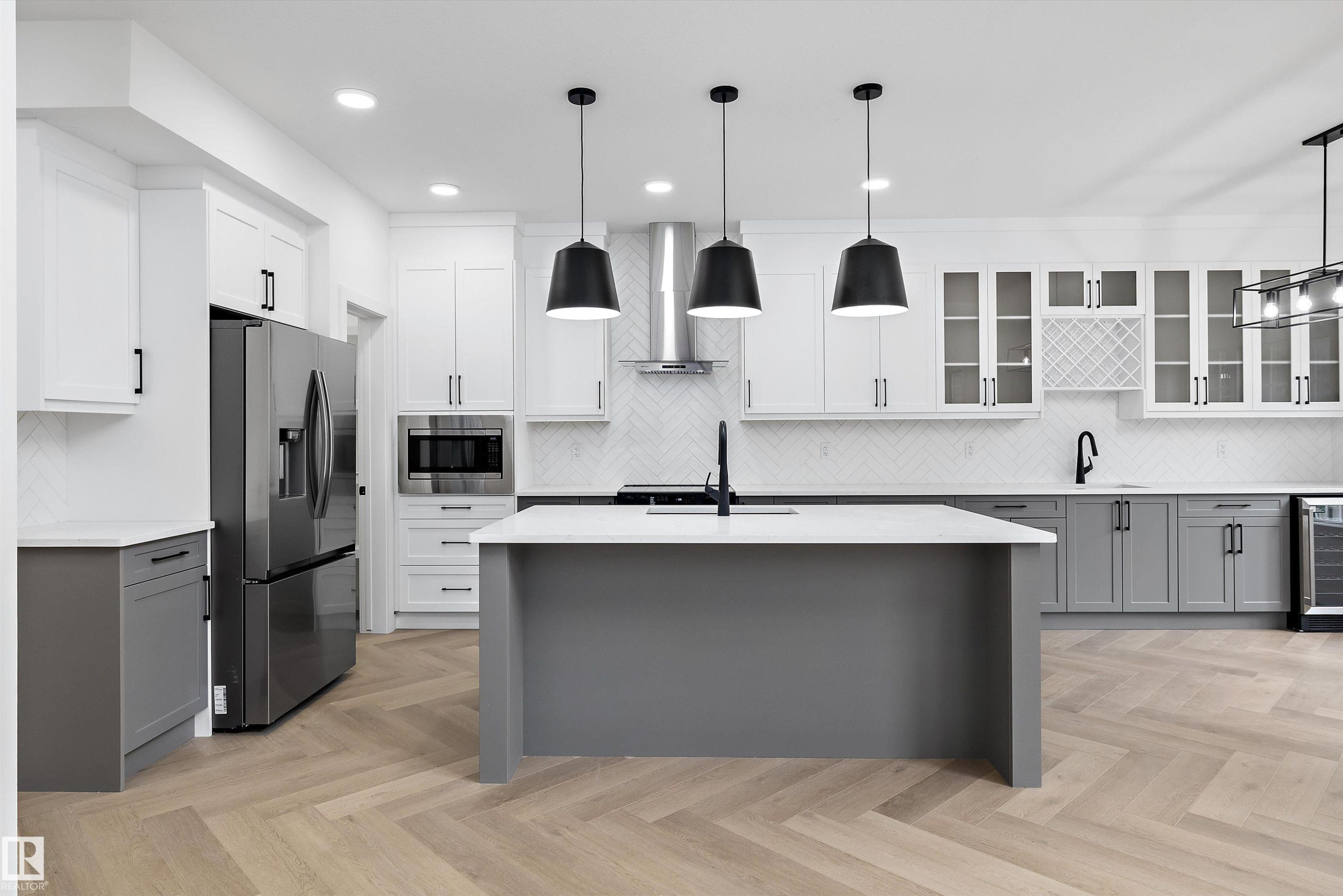 Modern kitchen featuring light wood-finish herringbone flooring, a spacious center island with a light-toned countertop, and two-tone cabinetry - 917 Elderberry Landing, Edmonton, AB