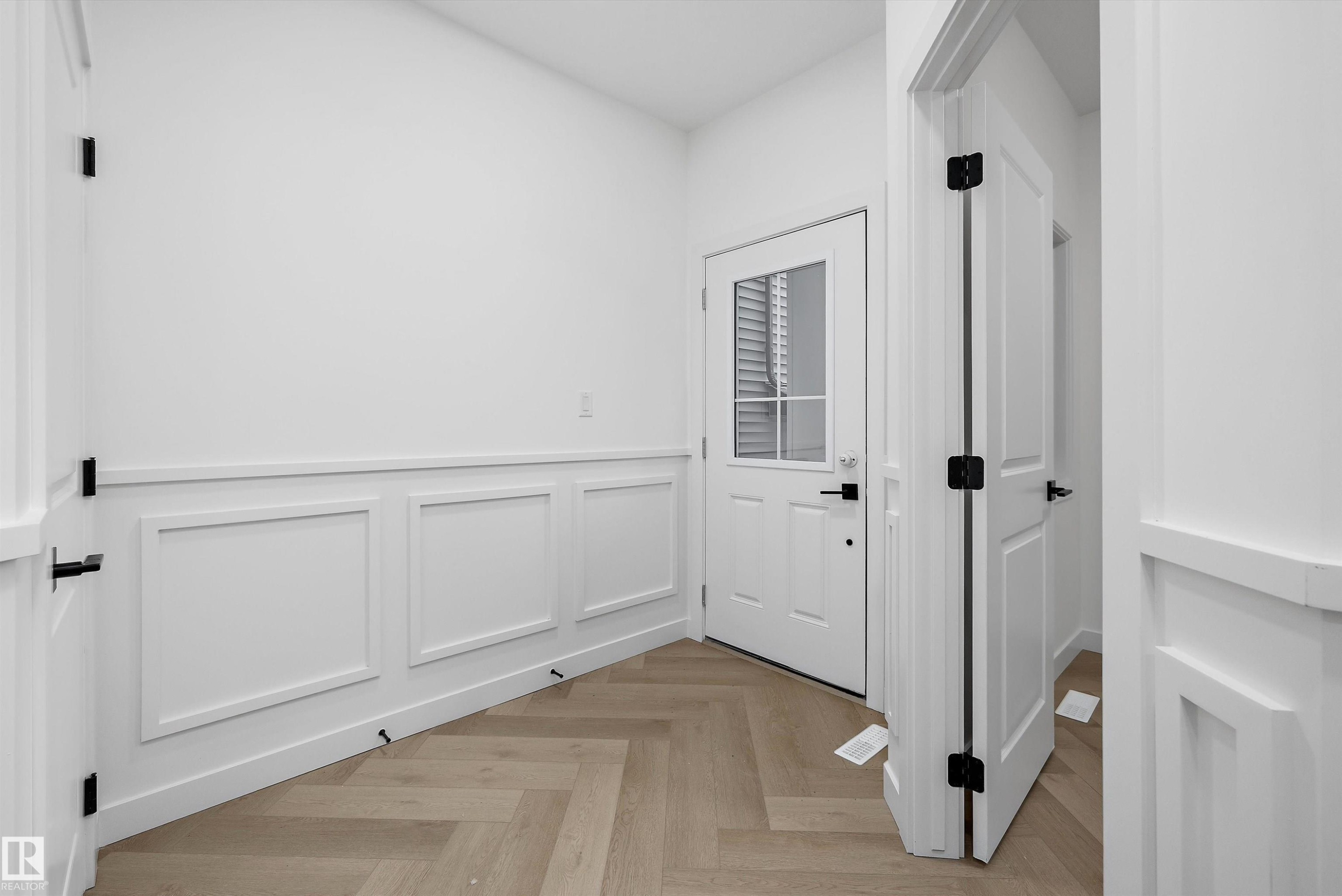 Entryway featuring a solid door with a paneled glass insert, white wainscoting, and wood-finish flooring in a herringbone pattern - 917 Elderberry Landing, Edmonton, AB