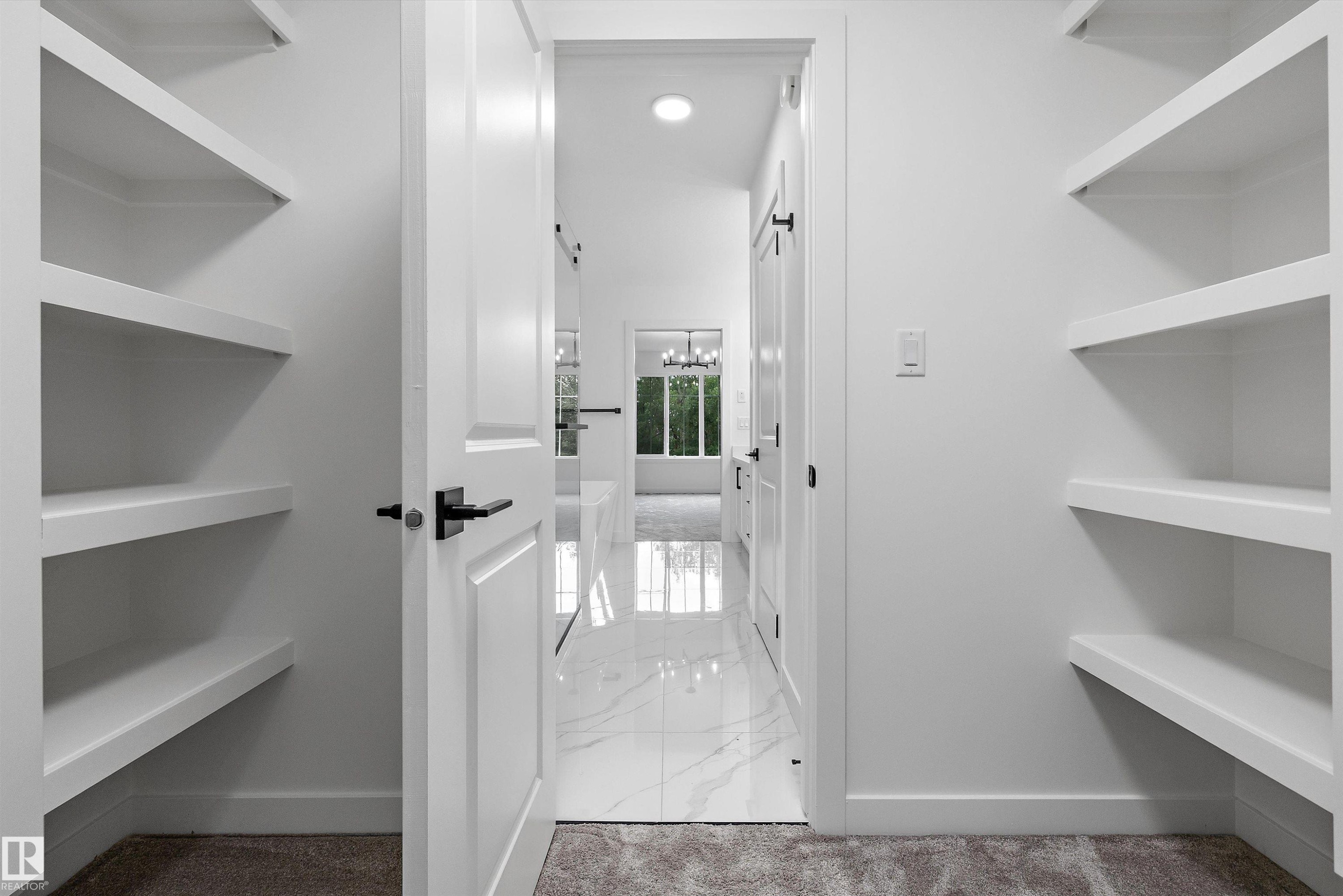 Walk-in closet featuring white shelving, light neutral carpet, and a white paneled door with black hardware - 917 Elderberry Landing, Edmonton, AB