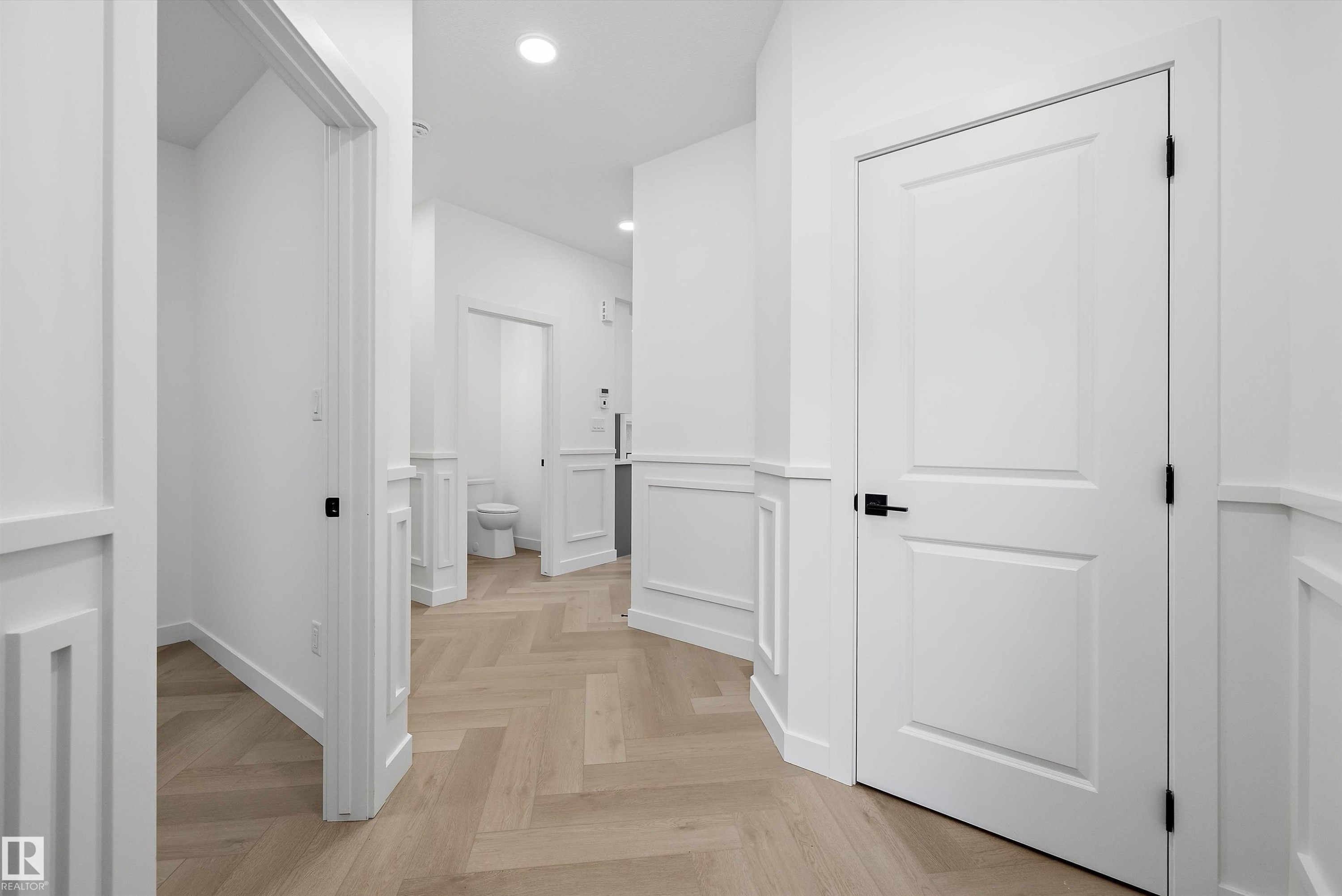 Hallway featuring herringbone wood-finish flooring, wainscoting, recessed lighting, and white paneled doors with matte black hardware - 917 Elderberry Landing, Edmonton, AB