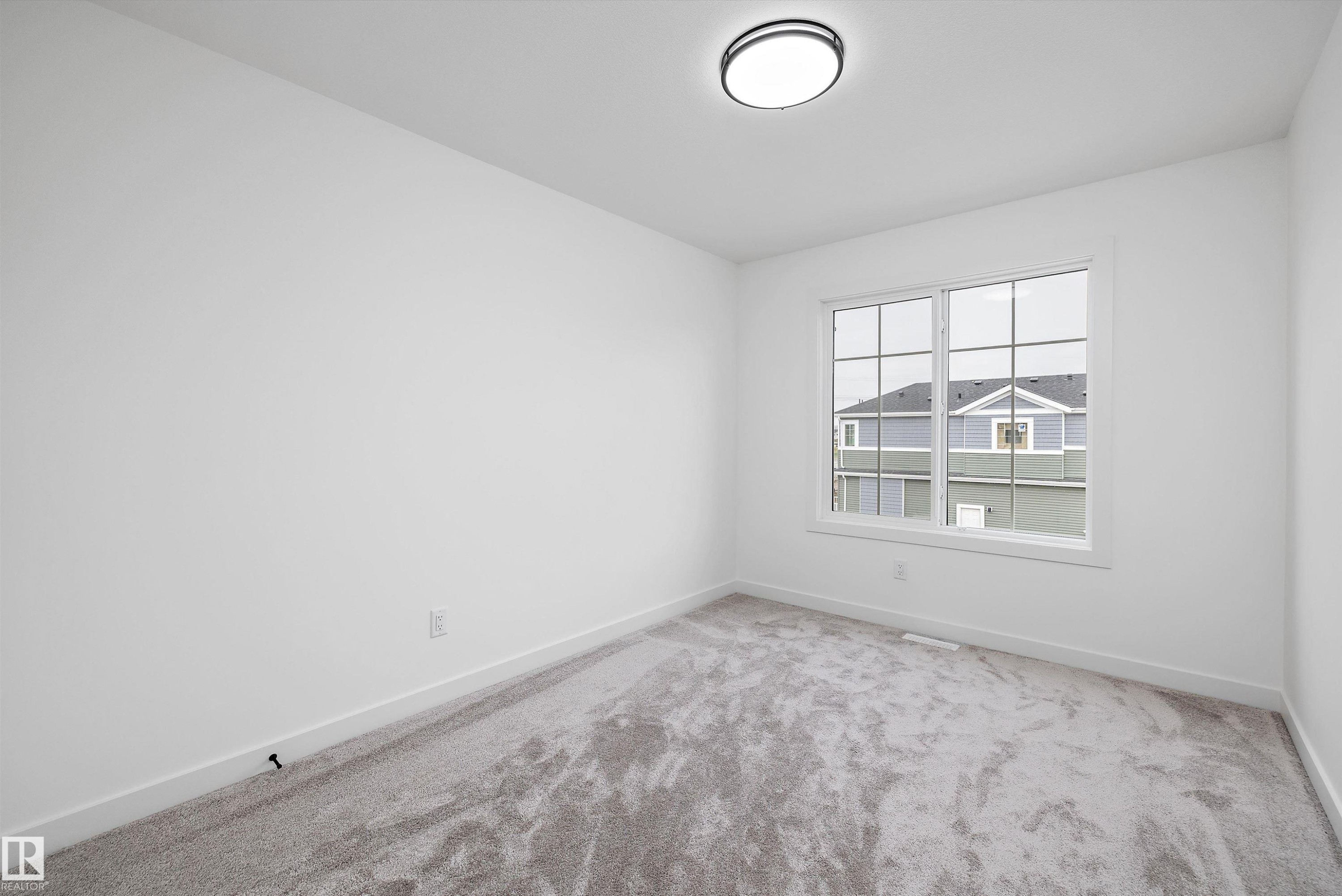Bright room featuring a multi-pane window with white trim, neutral carpet flooring, white walls, and a contemporary ceiling light fixture - 917 Elderberry Landing, Edmonton, AB