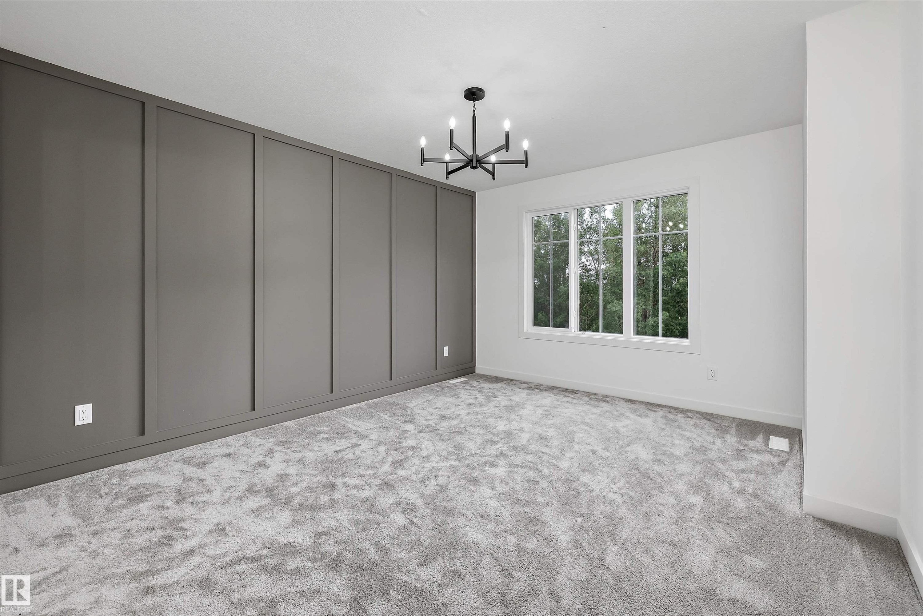 Room featuring a dark gray accent wall with vertical paneling, light gray carpeting, and a modern black chandelier - 917 Elderberry Landing, Edmonton, AB