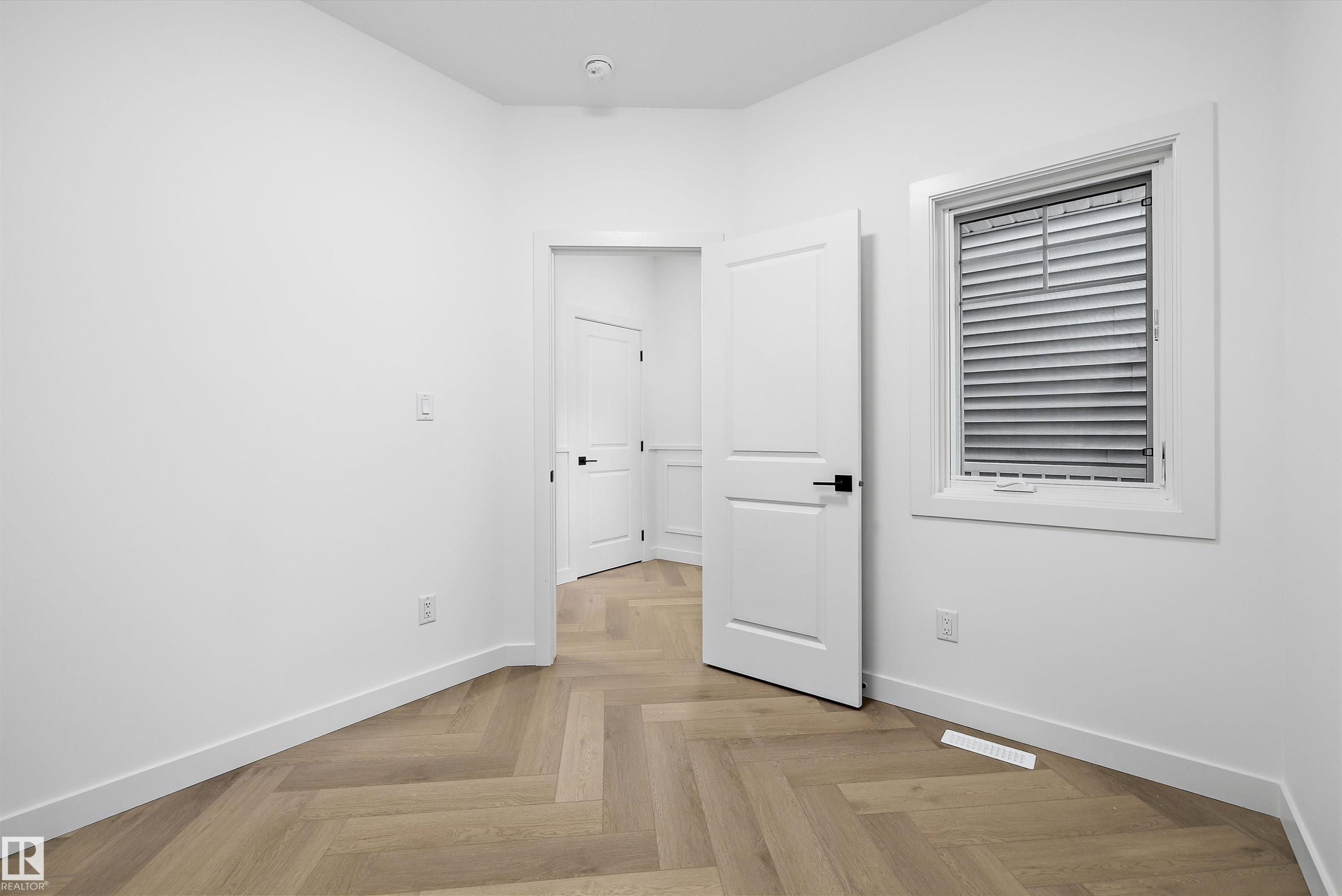 Interior room featuring herringbone wood-finish flooring, white baseboards, and a white interior door with black hardware - 917 Elderberry Landing, Edmonton, AB