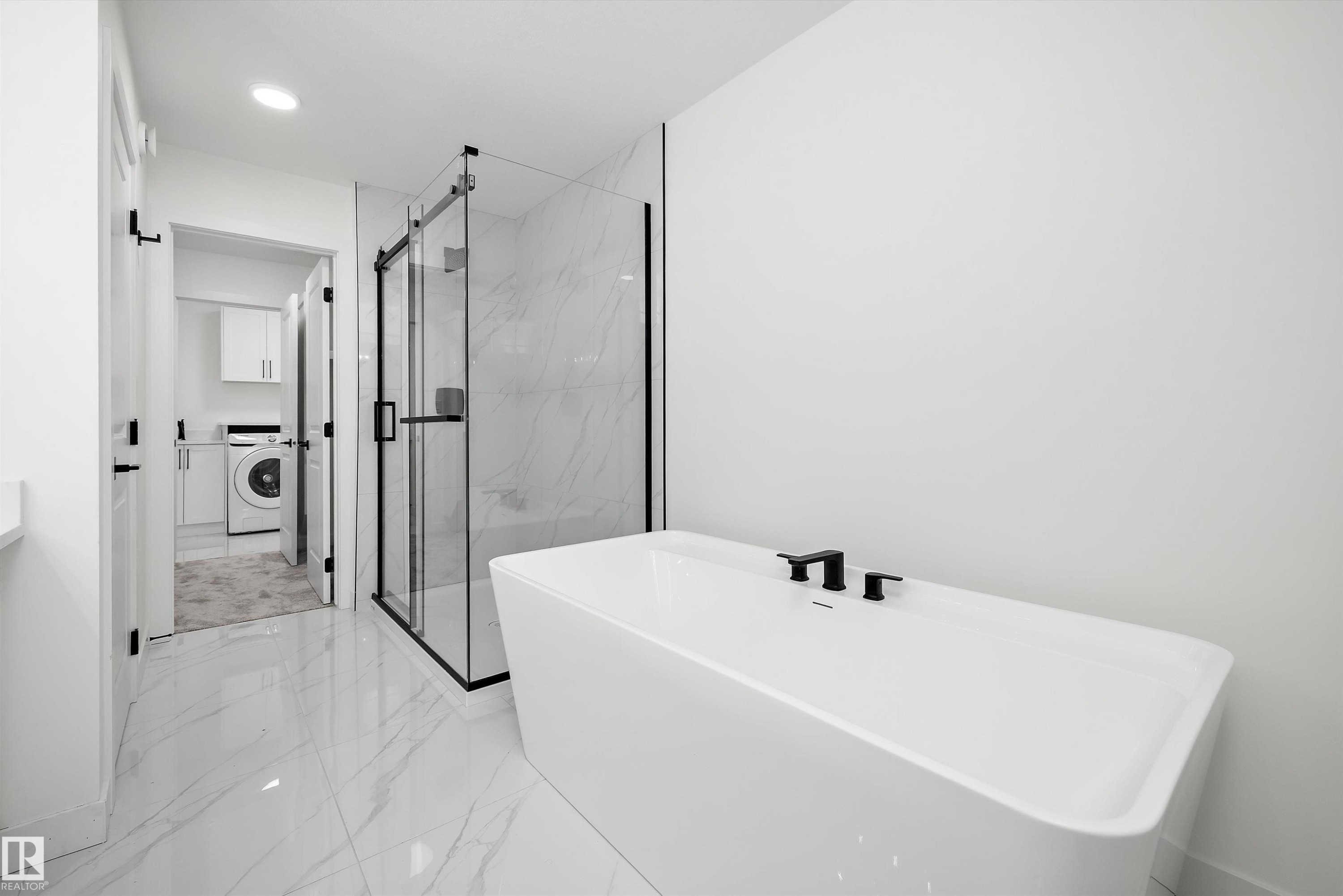 Modern bathroom featuring a freestanding tub with matte black fixtures, a glass-enclosed shower with black framing, and large-format tile flooring - 917 Elderberry Landing, Edmonton, AB
