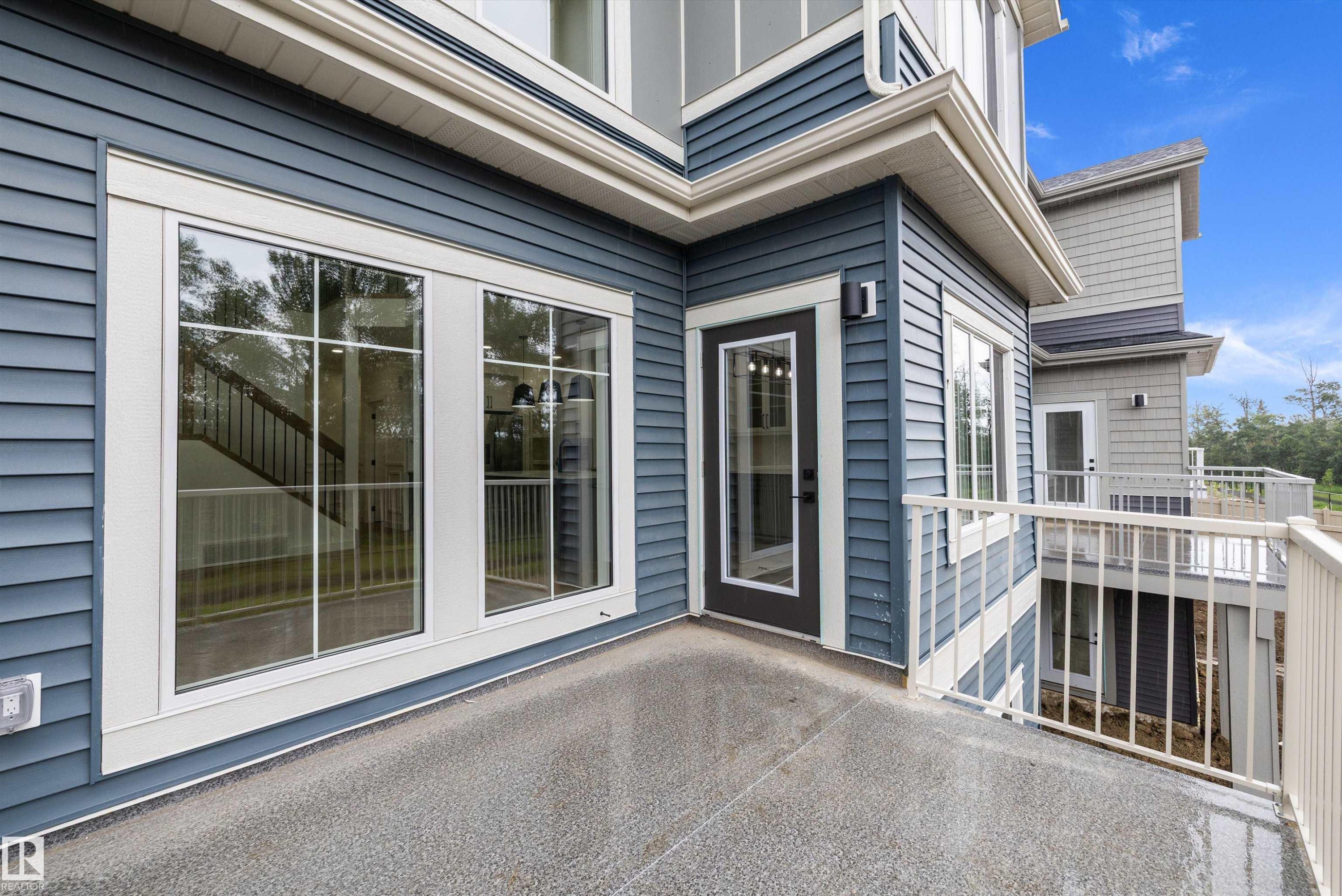 Private outdoor balcony featuring a textured concrete surface, white metal railing, and blue horizontal siding - 917 Elderberry Landing, Edmonton, AB
