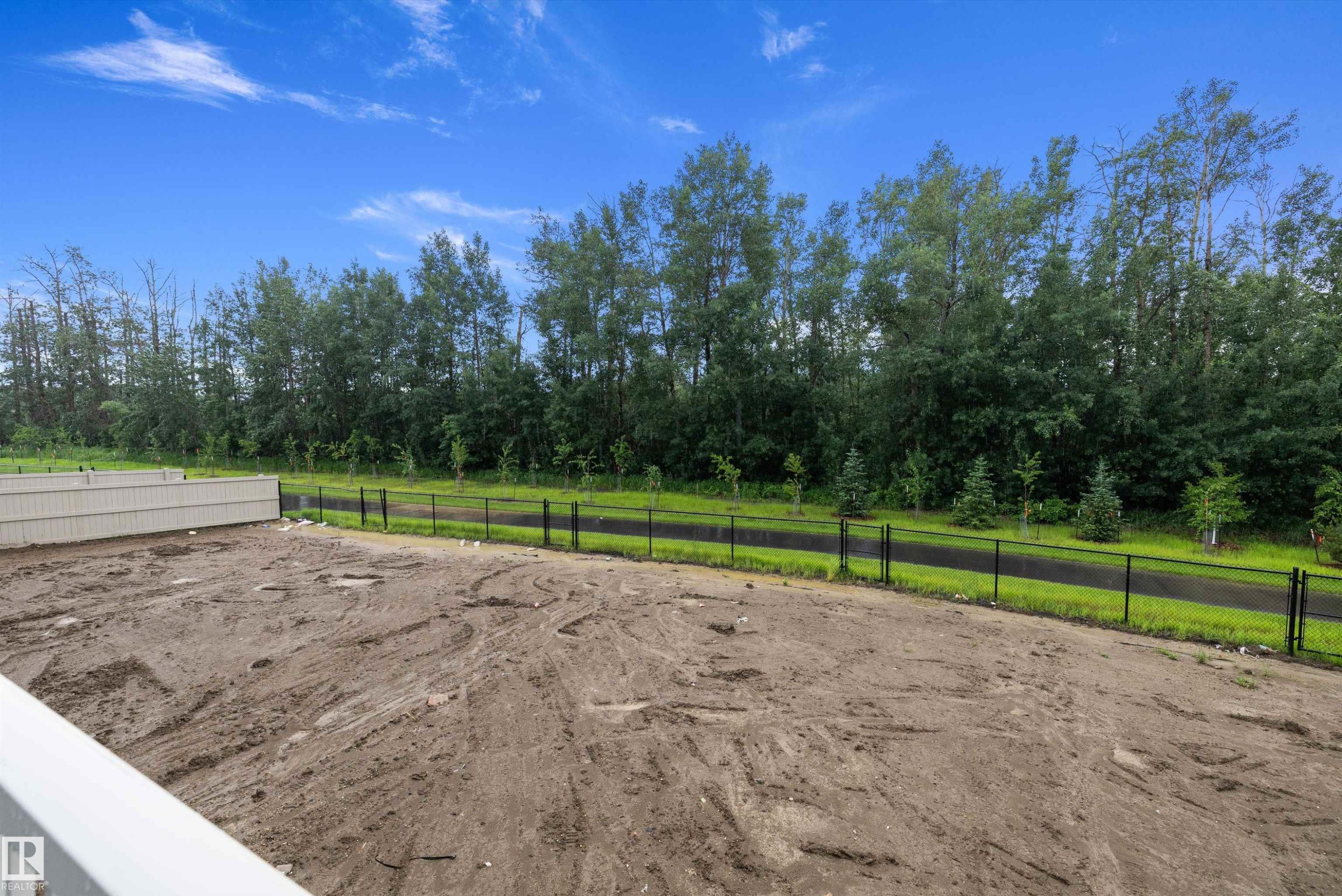 Spacious backyard with a dirt surface, bordered by a black metal fence - 917 Elderberry Landing, Edmonton, AB