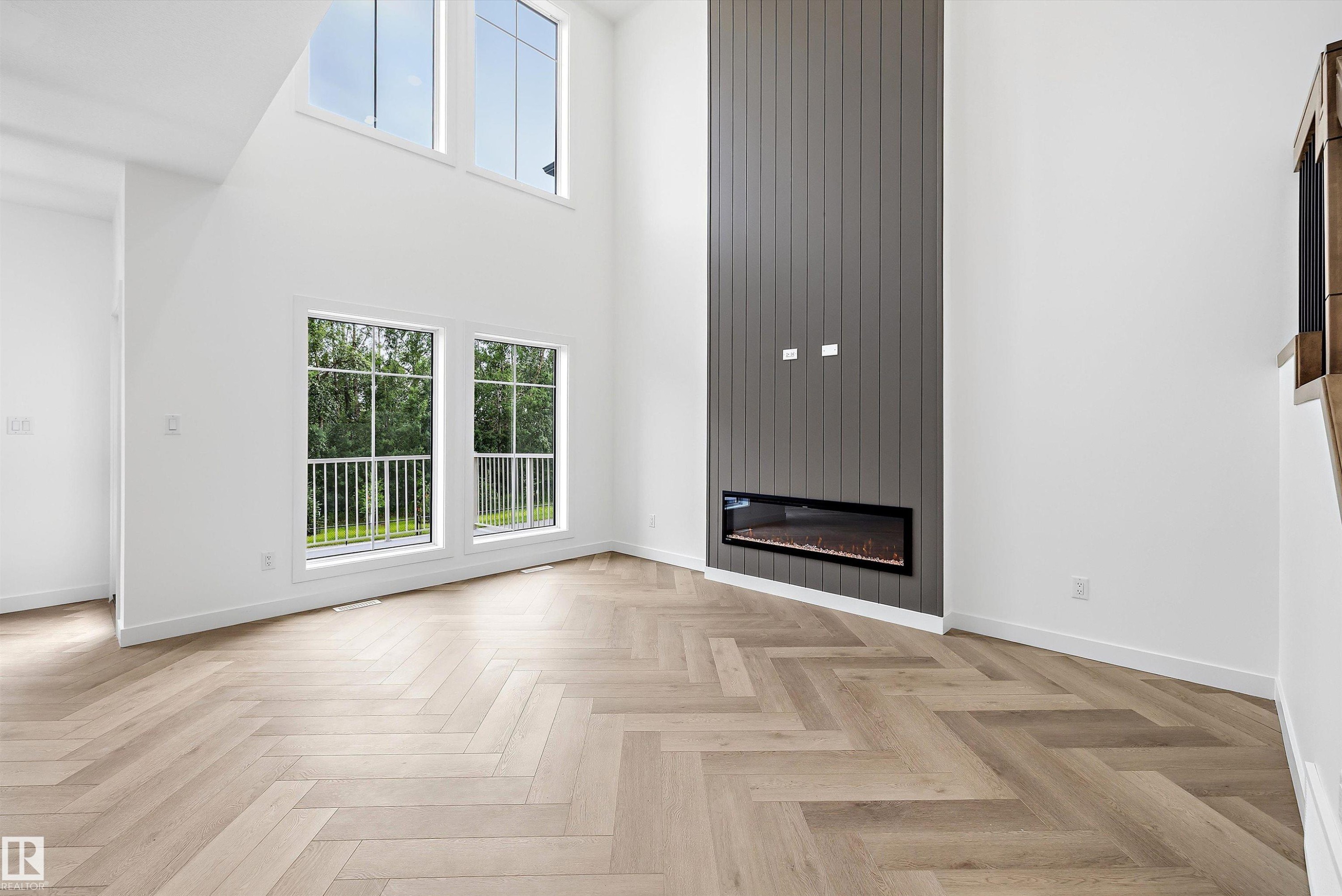 Spacious room featuring soaring ceilings, a modern linear electric fireplace with a vertical panel accent wall, and wood-finish flooring in a herringbone pattern - 917 Elderberry Landing, Edmonton, AB