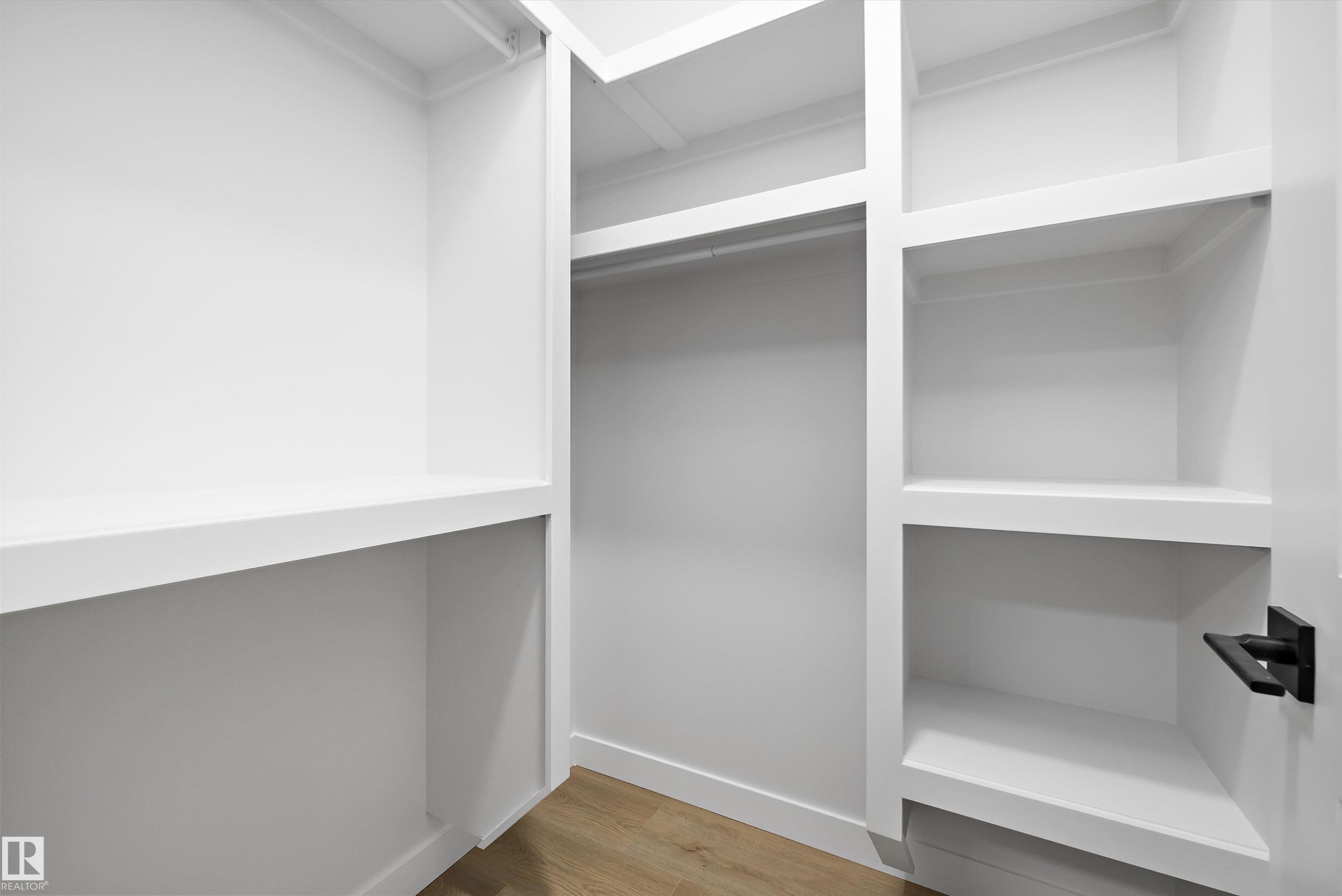 Custom closet system featuring white shelving, hanging rod, and wood-finish flooring - 954 Elderberry Landing, Edmonton, AB