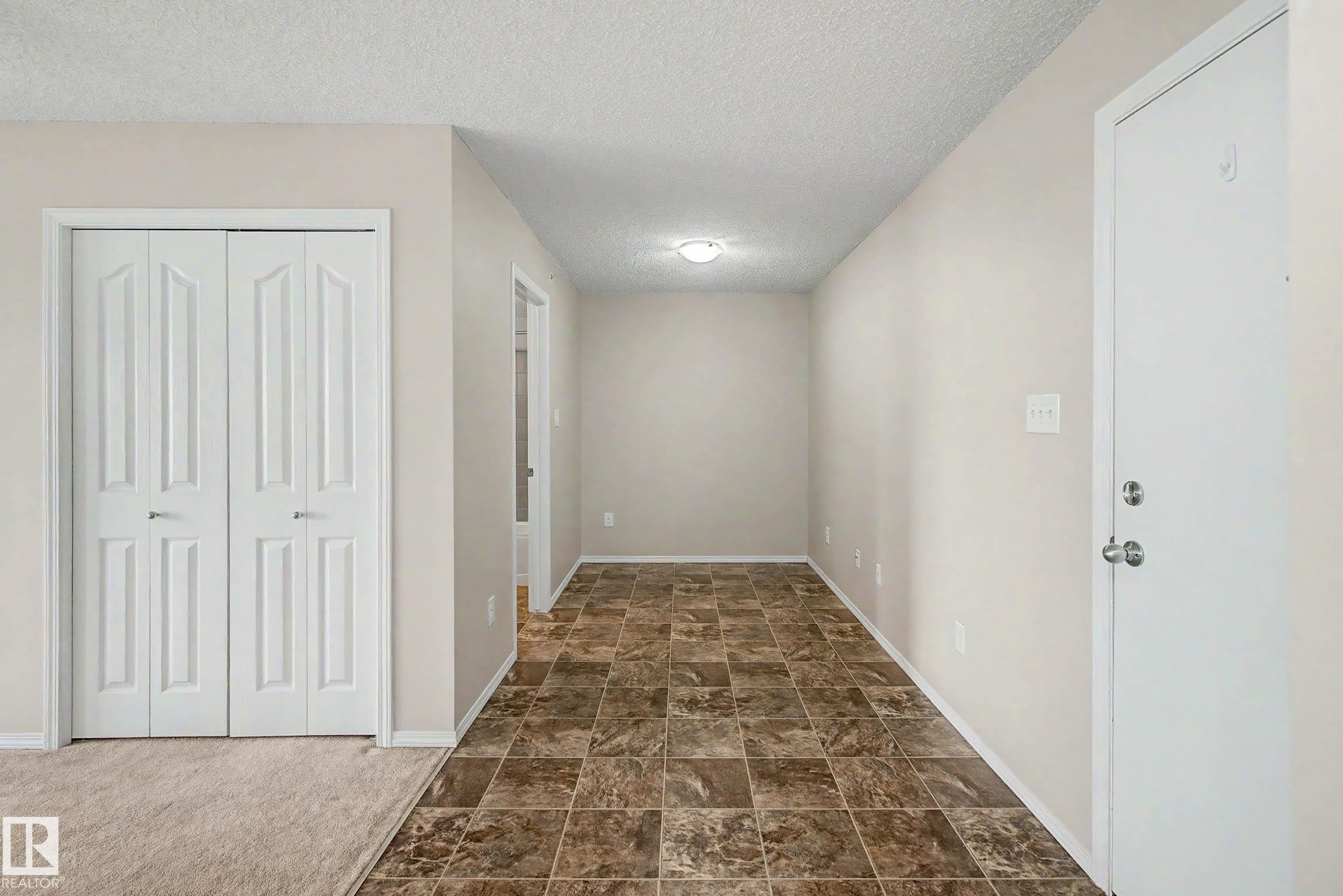 Entryway featuring a white paneled door, patterned floor tiles, and neutral wall paint - 404 1080 Mcconachie Boulevard, Edmonton, AB