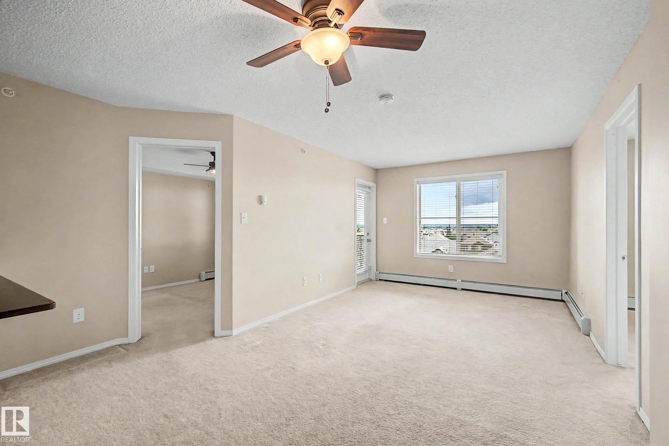Carpeted living space featuring a ceiling fan with light fixture, a window with blinds, and a door to an exterior balcony - 404 1080 Mcconachie Boulevard, Edmonton, AB