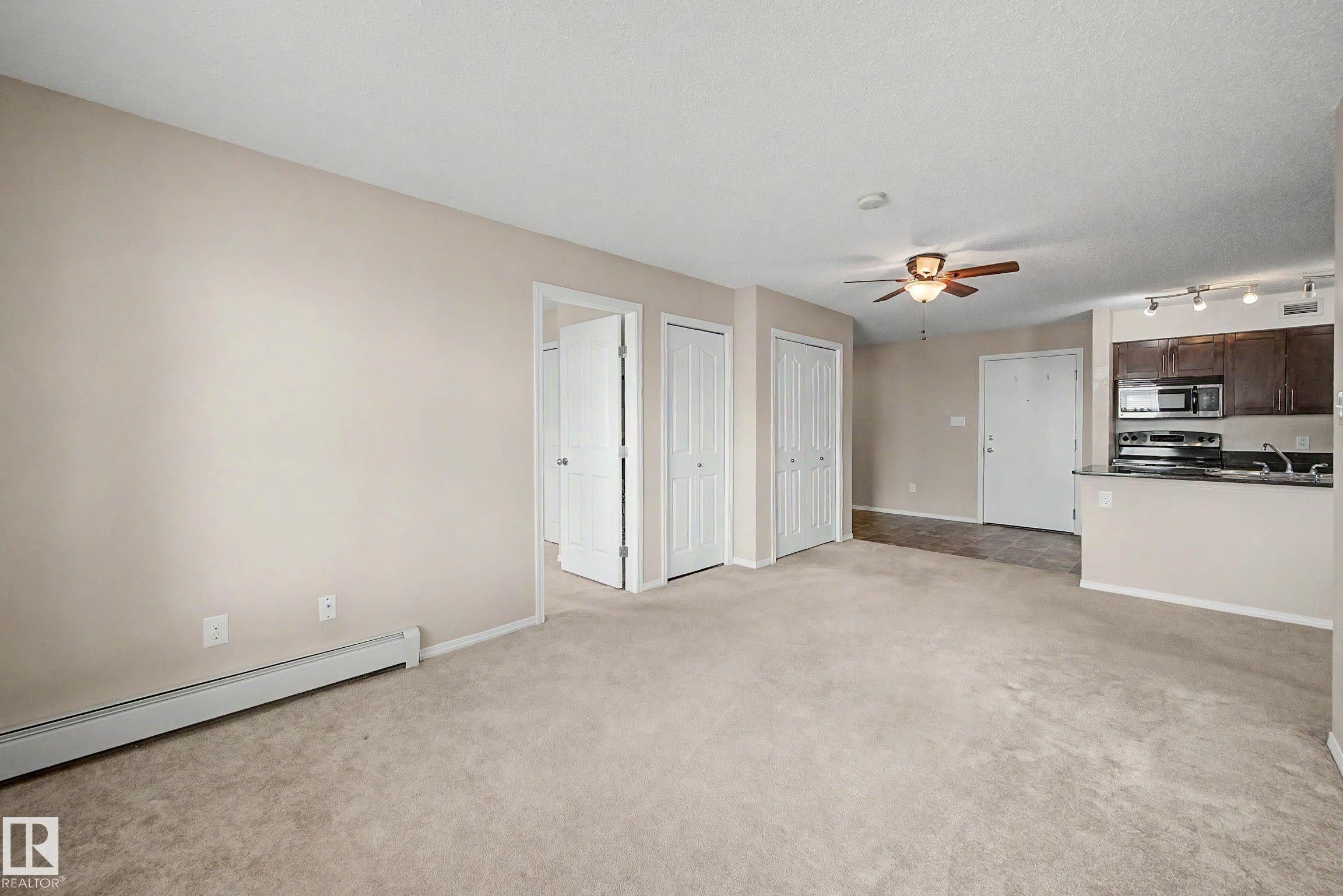 Carpeted living area featuring a ceiling fan, baseboard heating, and direct access to the kitchen space - 404 1080 Mcconachie Boulevard, Edmonton, AB