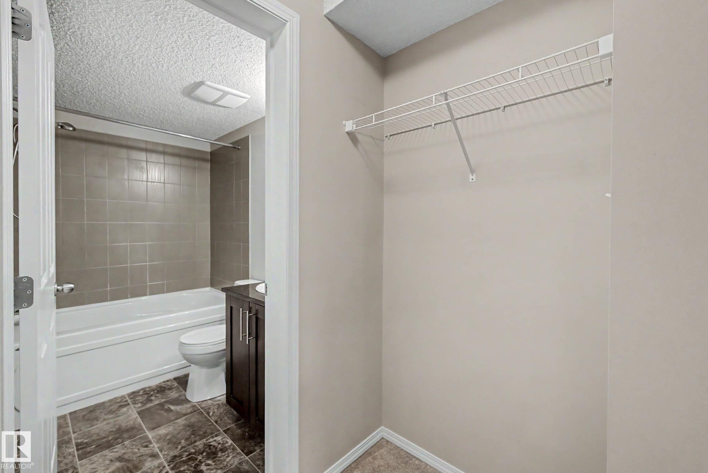 Bathroom featuring a white bathtub with neutral-toned tiled surround, a dark wood-finish vanity, and patterned tile flooring - 404 1080 Mcconachie Boulevard, Edmonton, AB