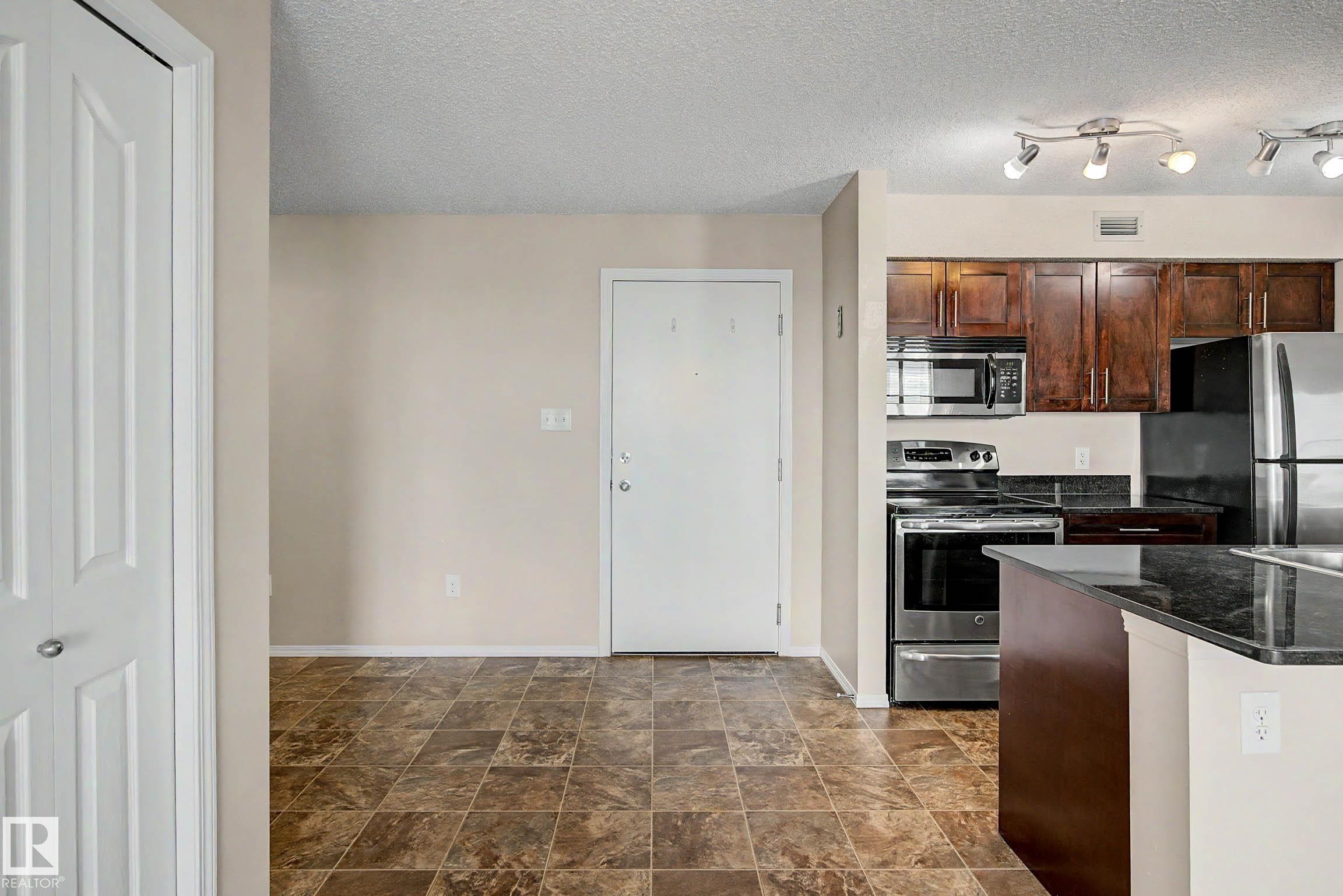 Kitchen featuring stainless steel appliances, dark wood cabinetry, and a black countertop - 404 1080 Mcconachie Boulevard, Edmonton, AB
