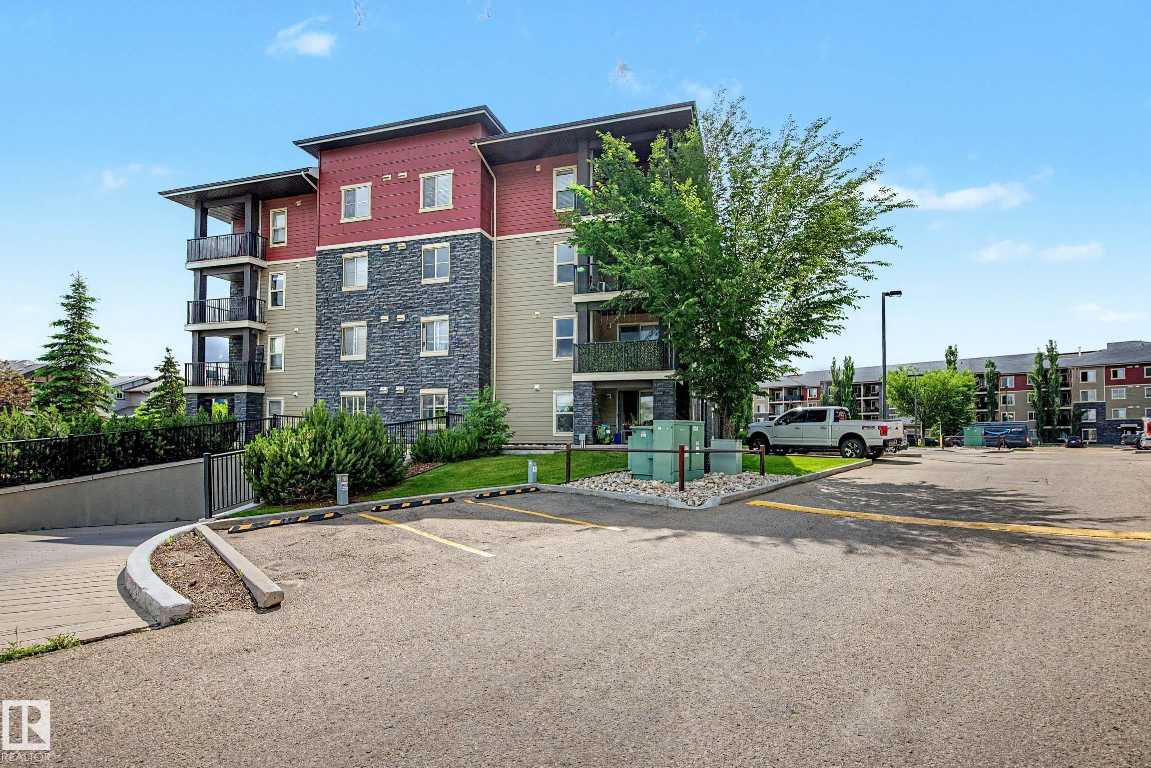 Multi-story residential building featuring a stone facade, red siding, and multiple balconies with dark railings - 404 1080 Mcconachie Boulevard, Edmonton, AB