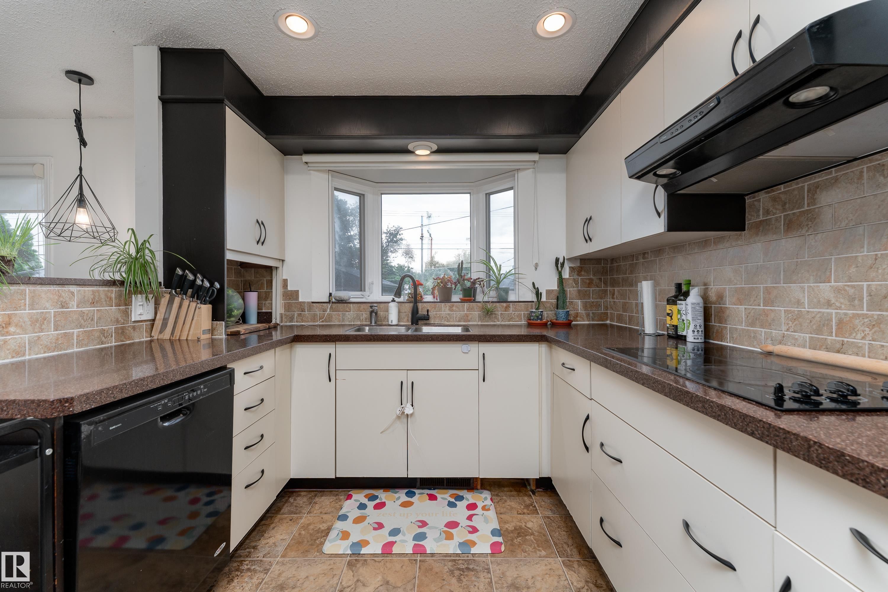 U-shaped kitchen featuring white cabinetry, dark countertops, a tile backsplash, recessed lighting, and a bay window - 13616 137 Street, Edmonton, AB