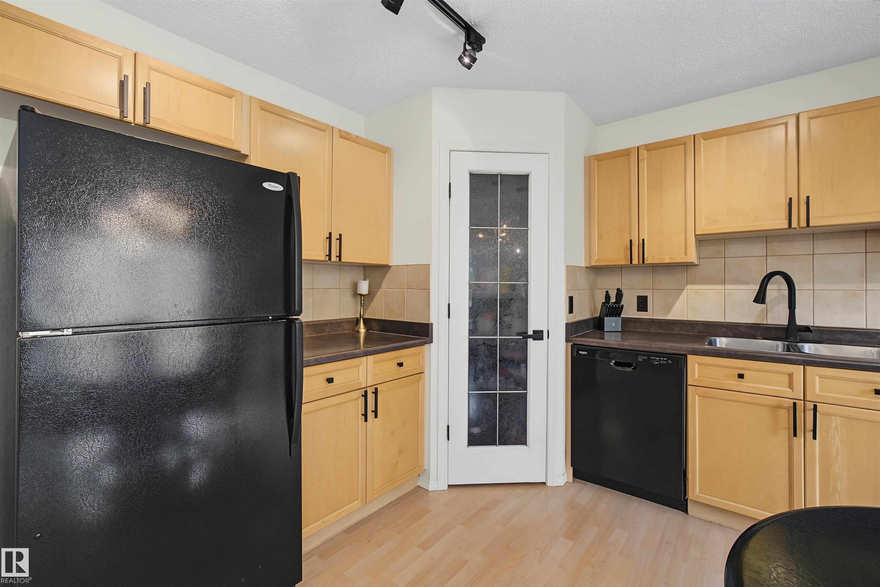 Kitchen featuring light wood-finish cabinetry with dark hardware, dark countertops, and black appliances - 15 450 Hyndman Crescent, Edmonton, AB