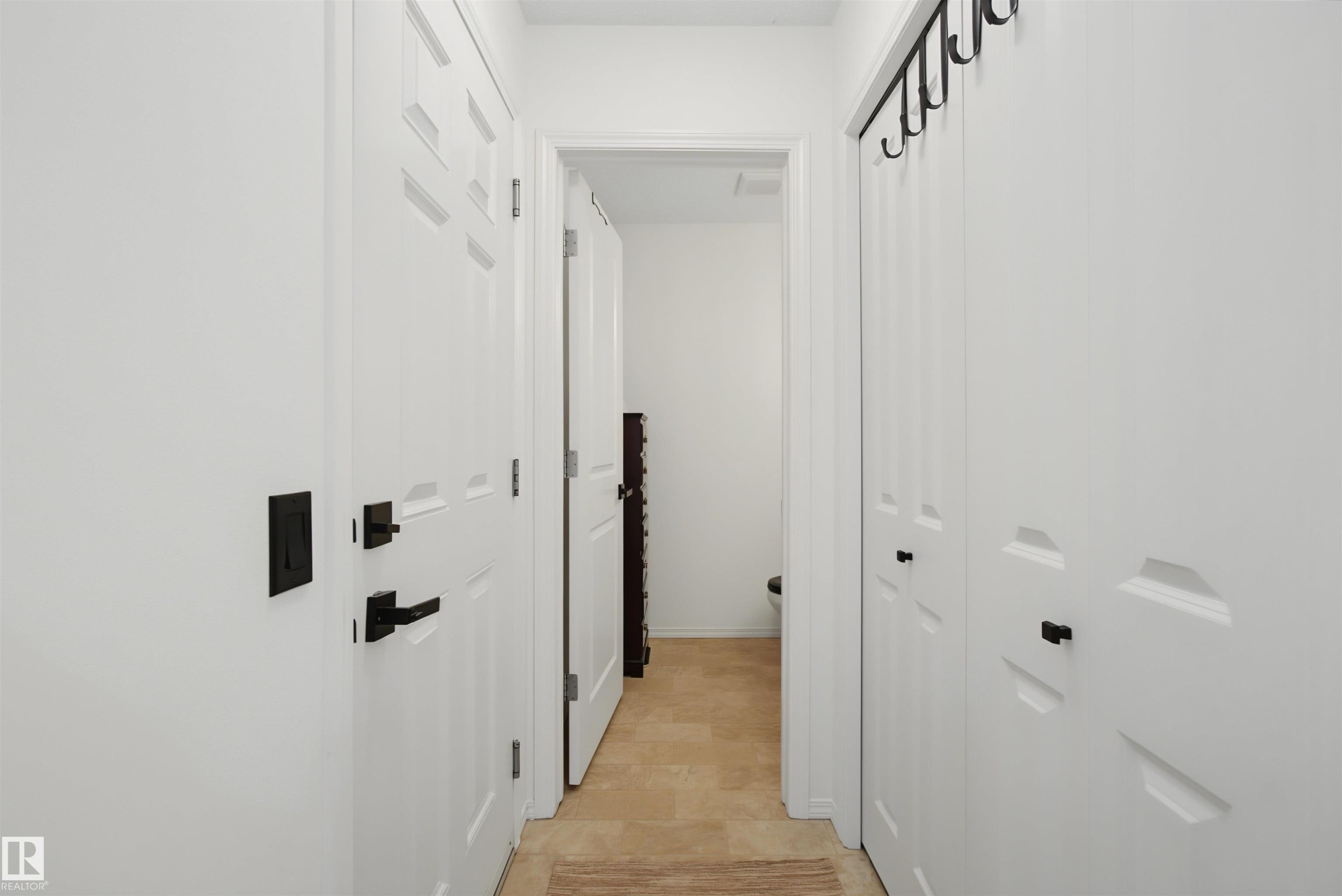Hallway featuring white paneled doors with matte black hardware - 15 450 Hyndman Crescent, Edmonton, AB