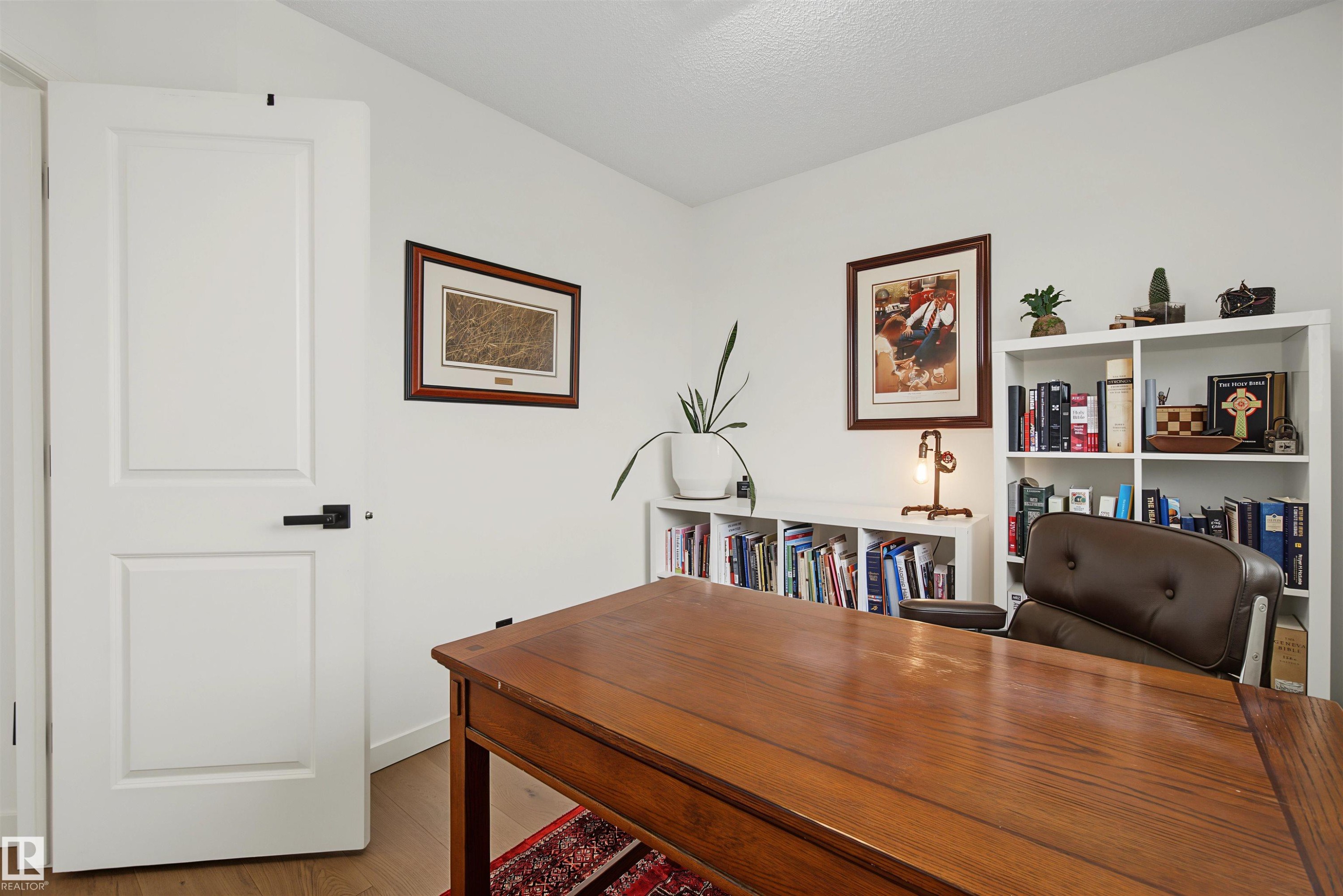 Dedicated room featuring wood-finish flooring, crisp white walls, a solid panel door with dark hardware, and built-in shelving - 15 450 Hyndman Crescent, Edmonton, AB