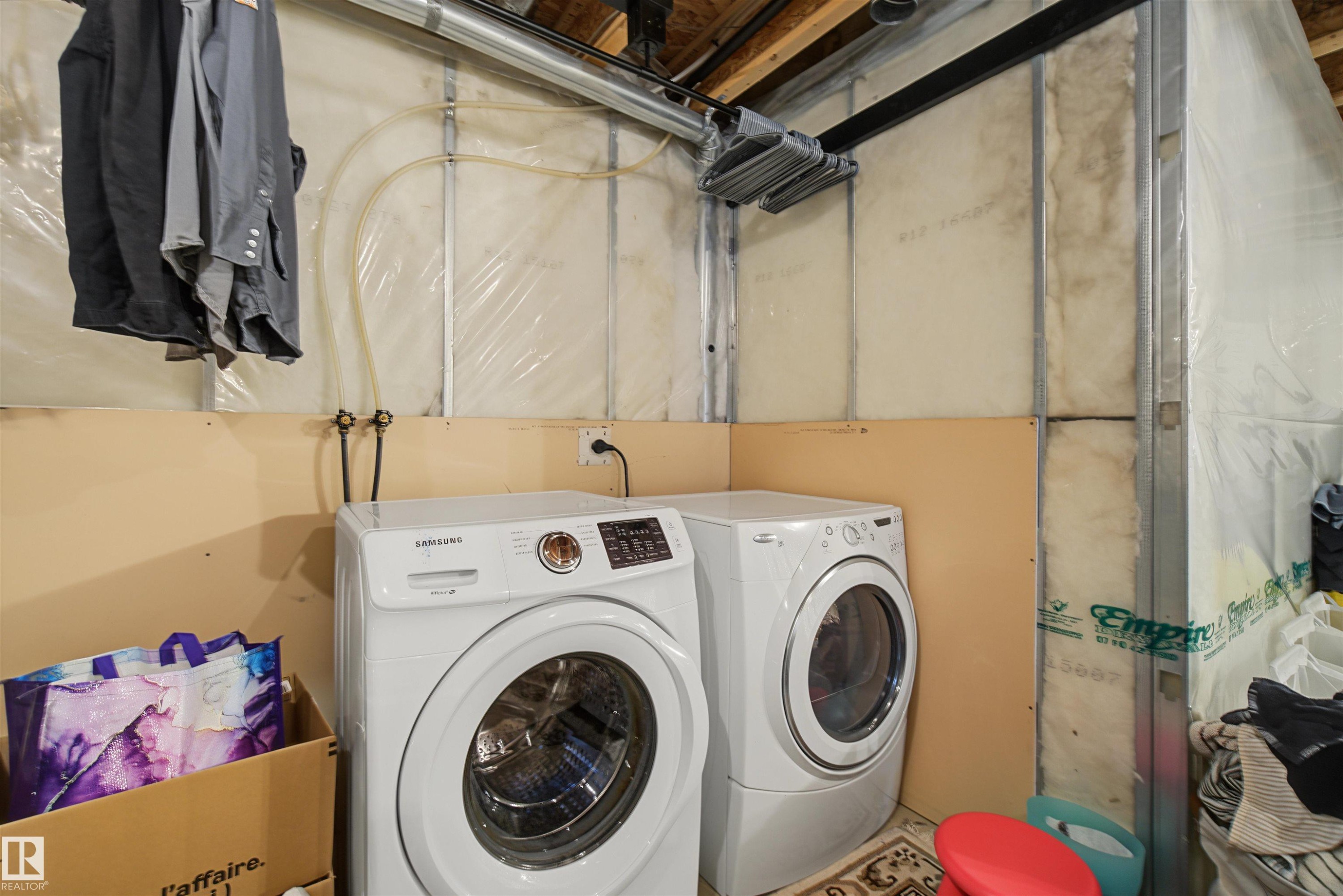 Dedicated laundry area with a washer and dryer, exposed ceiling joists, and insulated wall sections - 15 450 Hyndman Crescent, Edmonton, AB