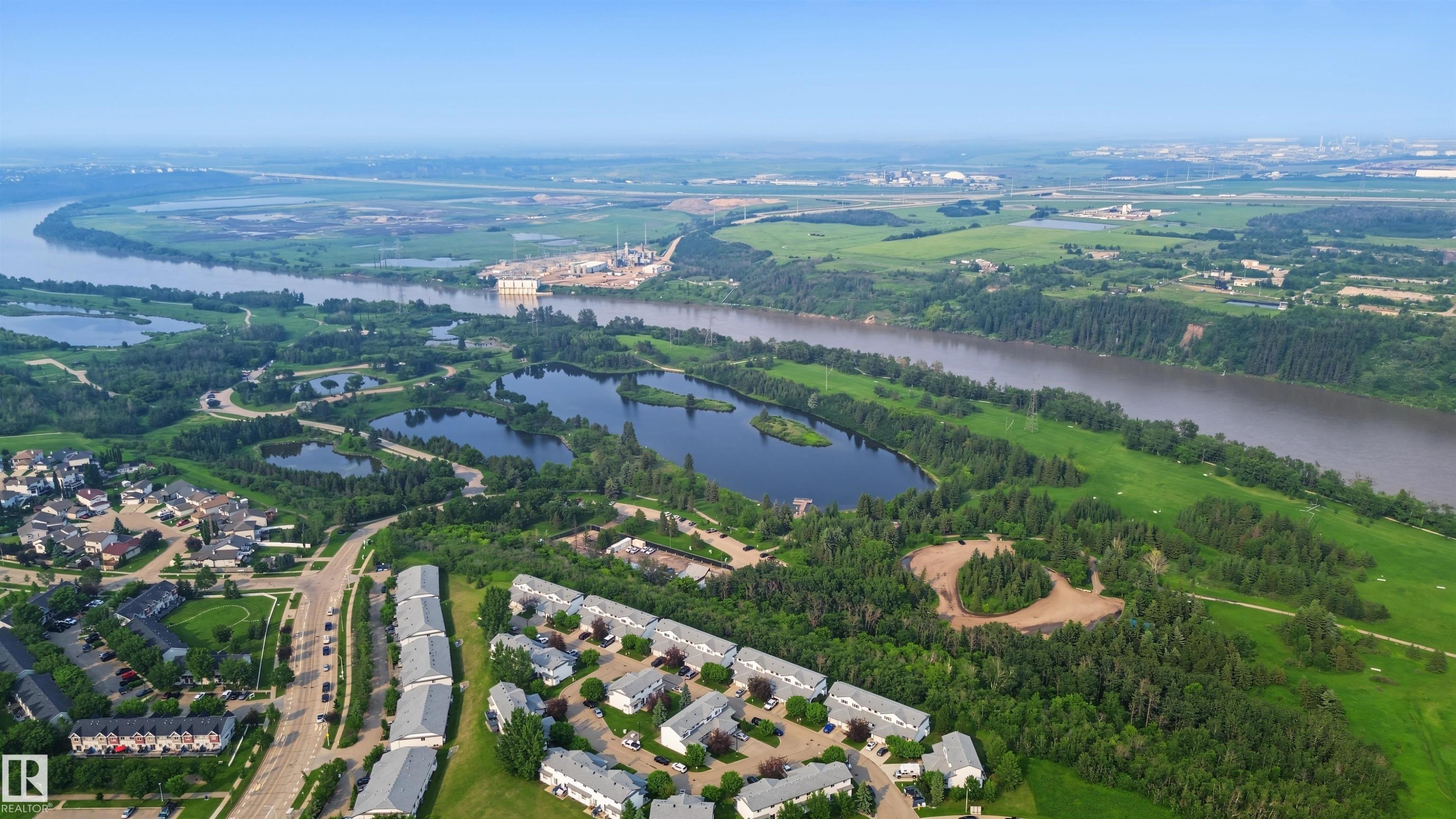 Aerial perspective showcasing multiple residential developments surrounded by extensive green spaces, a winding river, and several natural ponds - 15 450 Hyndman Crescent, Edmonton, AB