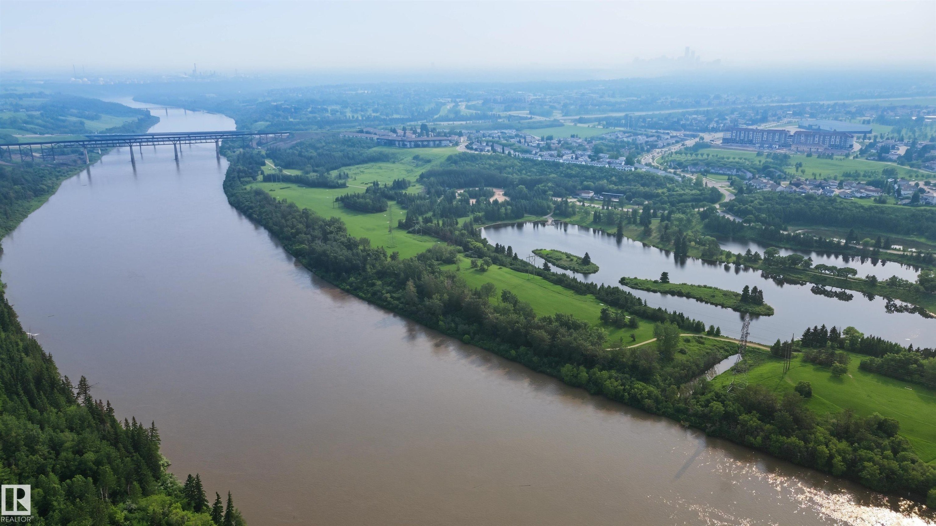 Expansive riverfront property featuring a winding waterway, lush green banks, and mature tree lines - 15 450 Hyndman Crescent, Edmonton, AB