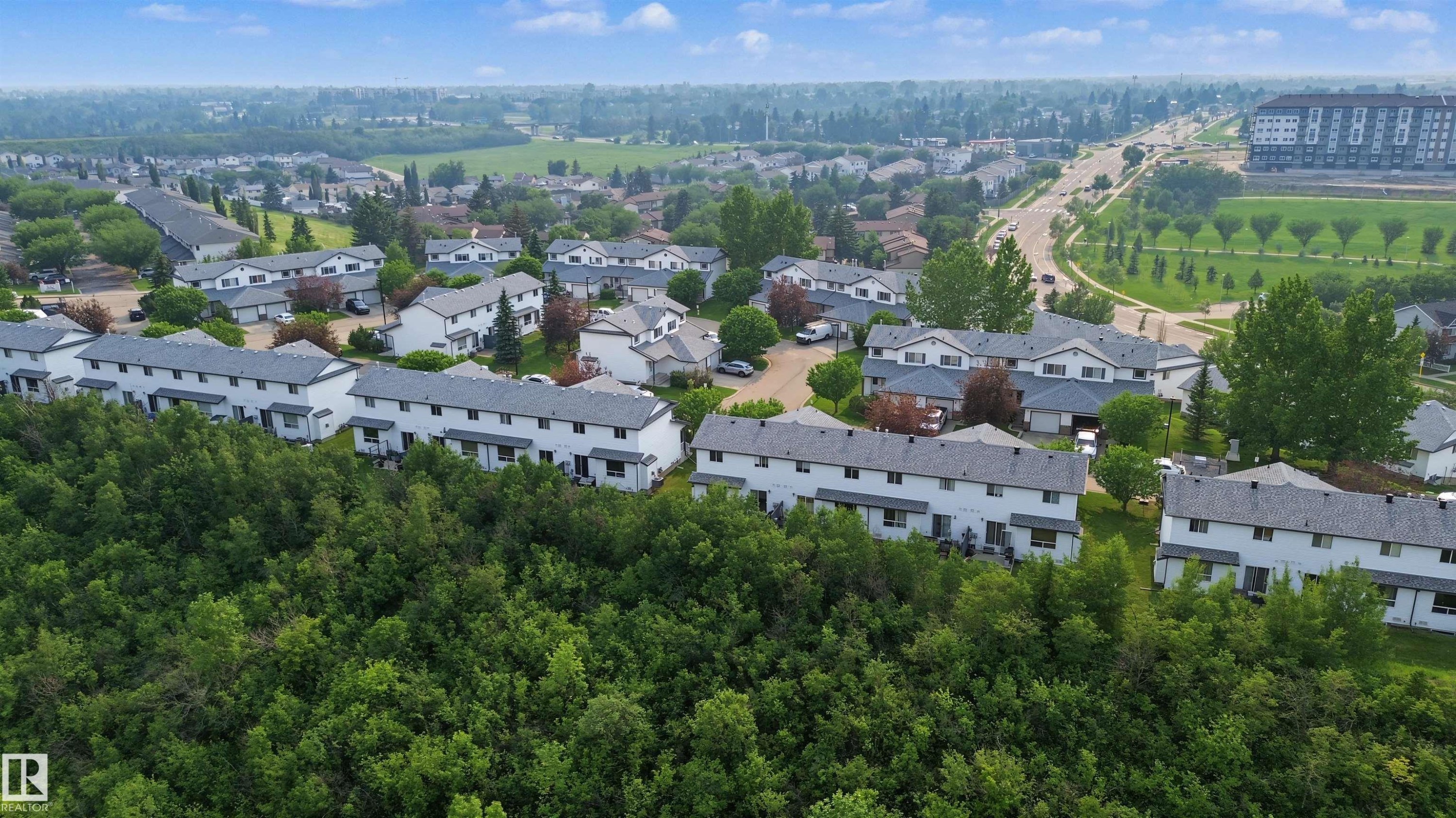 Townhome community featuring multiple two-story residences with light-colored siding and gray shingle roofs - 15 450 Hyndman Crescent, Edmonton, AB