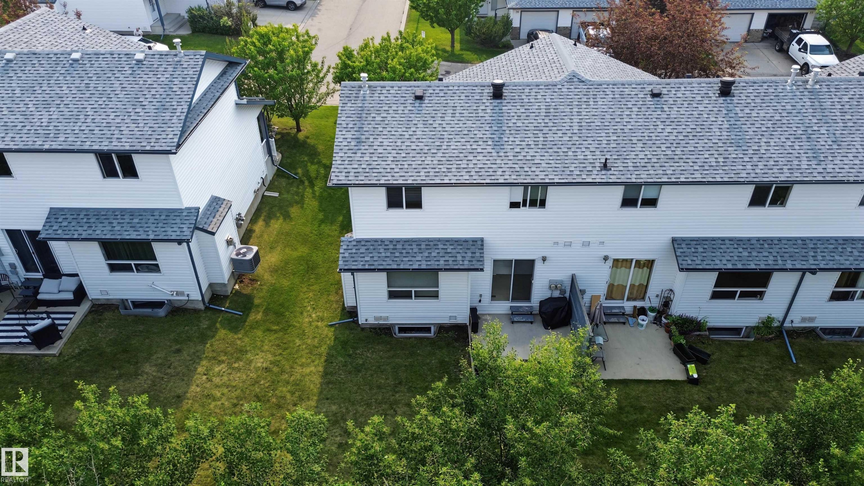 Rear exterior featuring white siding, a gray shingle roof, and multiple windows - 15 450 Hyndman Crescent, Edmonton, AB