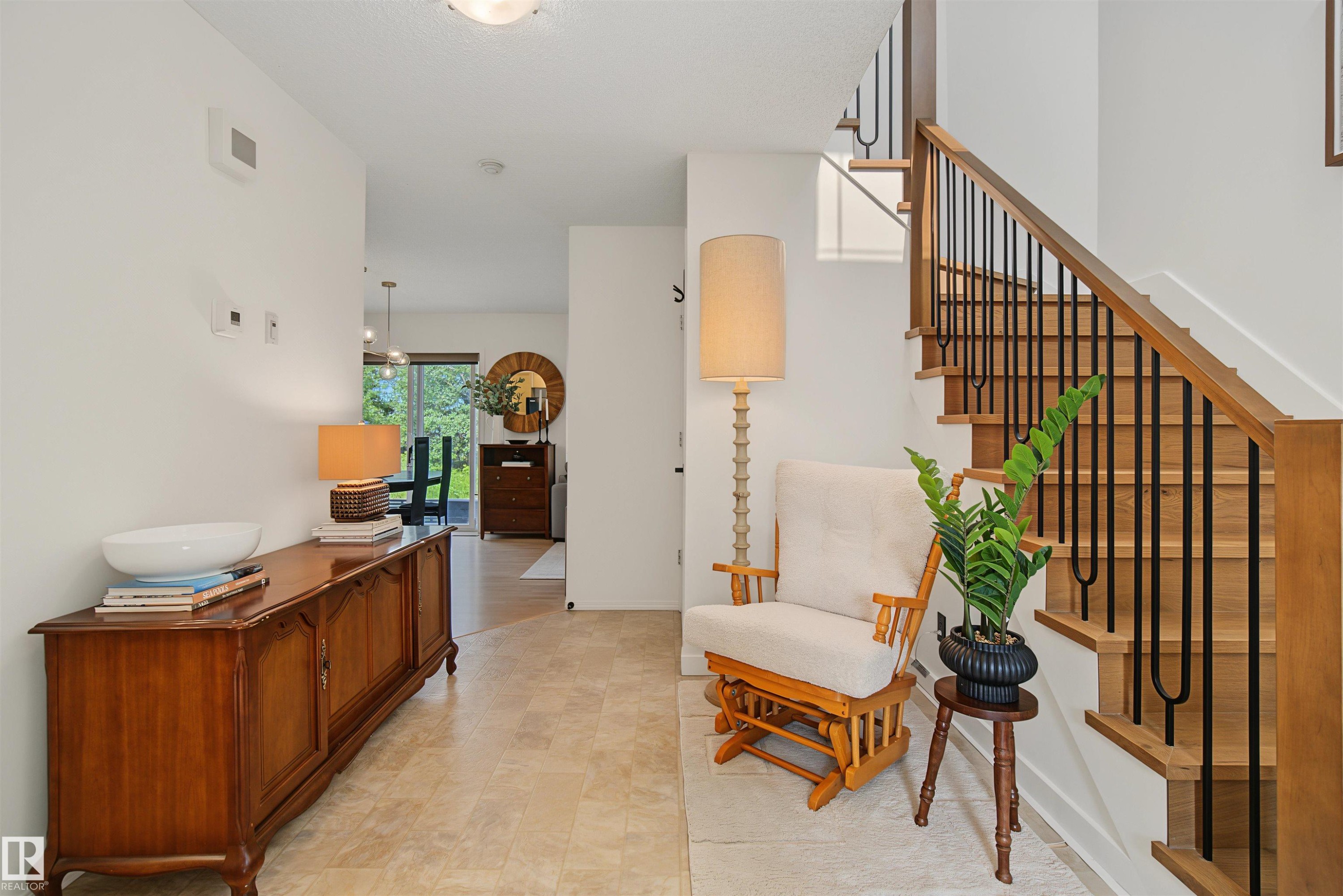Entryway featuring light-toned tile flooring and a wood staircase with black iron balusters - 15 450 Hyndman Crescent, Edmonton, AB
