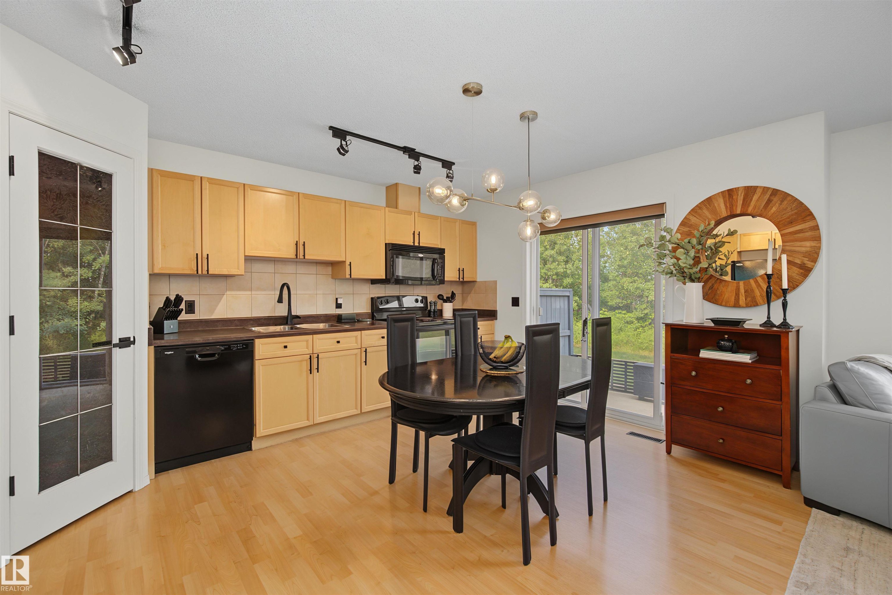 Open-concept kitchen featuring light wood cabinetry, black appliances, and a tile backsplash - 15 450 Hyndman Crescent, Edmonton, AB