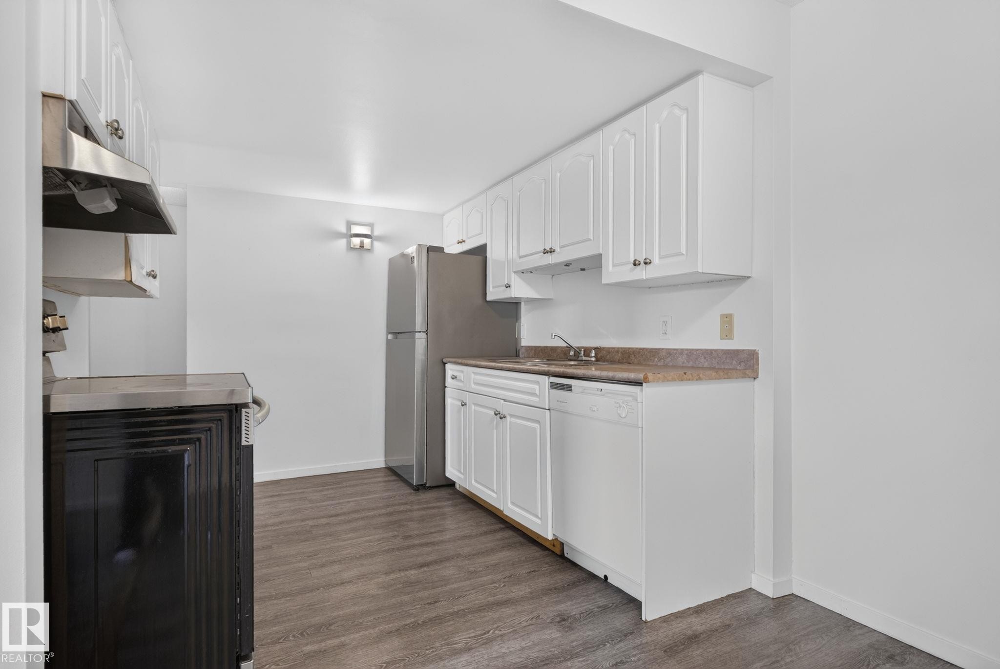 Kitchen featuring white cabinetry, a built-in stainless steel range hood, a stainless steel refrigerator, a dishwasher, and wood-finish flooring - 401 2908 116A Avenue, Edmonton, AB