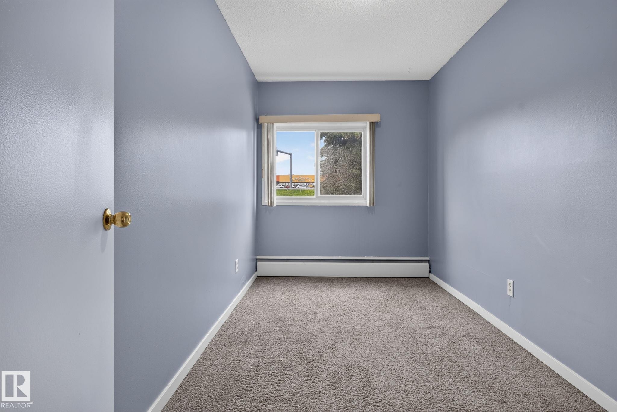 Carpeted interior room featuring light blue walls, white trim, and a window with a valance - 401 2908 116A Avenue, Edmonton, AB