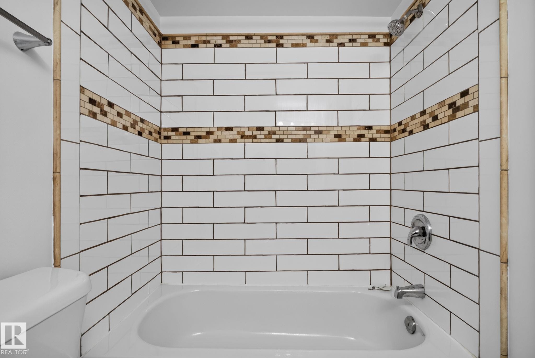 Bathtub with white subway tile surround, featuring two decorative mosaic tile accent bands - 401 2908 116A Avenue, Edmonton, AB