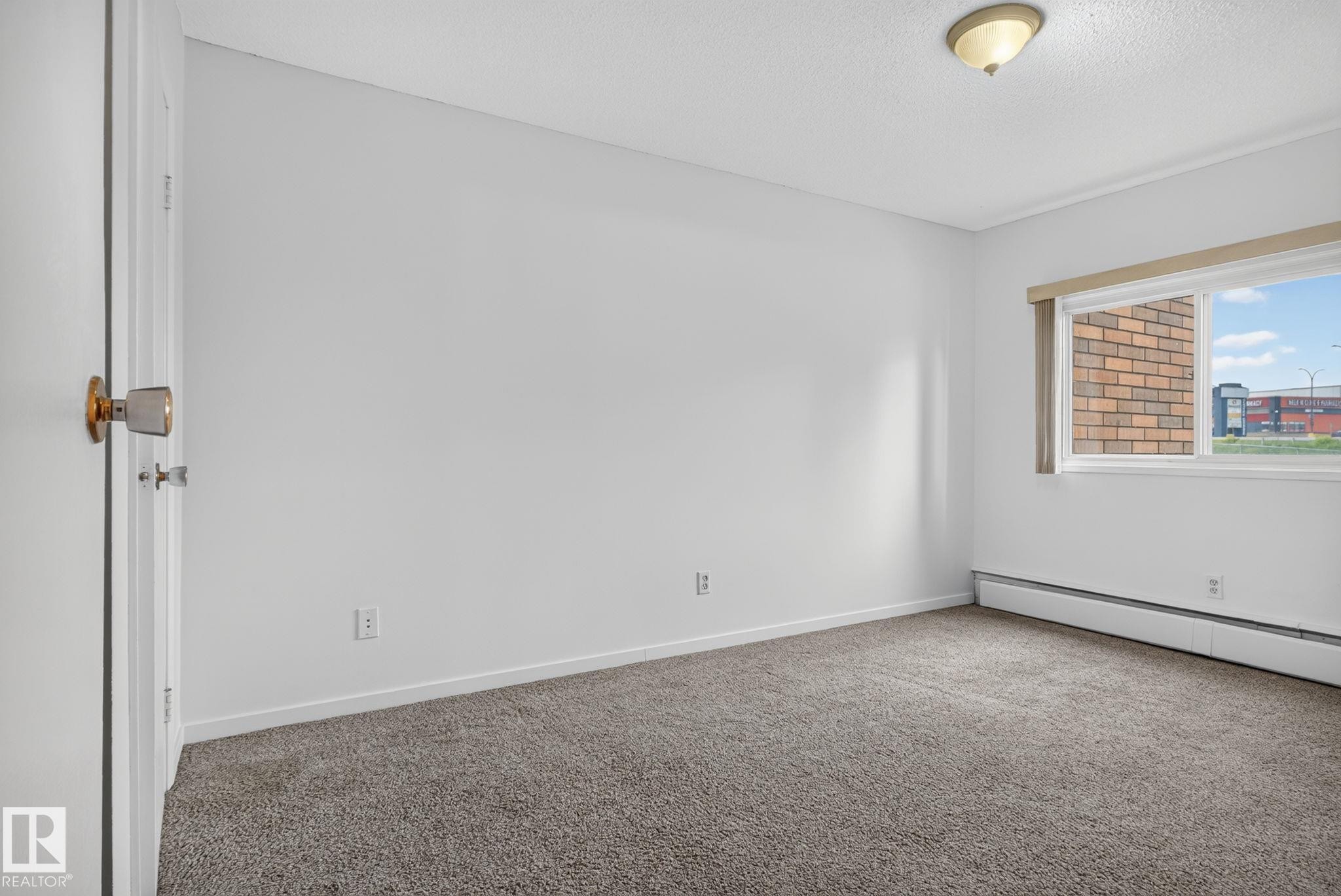 Neutral-toned room featuring a window with a valance, baseboard heating, textured ceiling, and gray carpet flooring - 401 2908 116A Avenue, Edmonton, AB