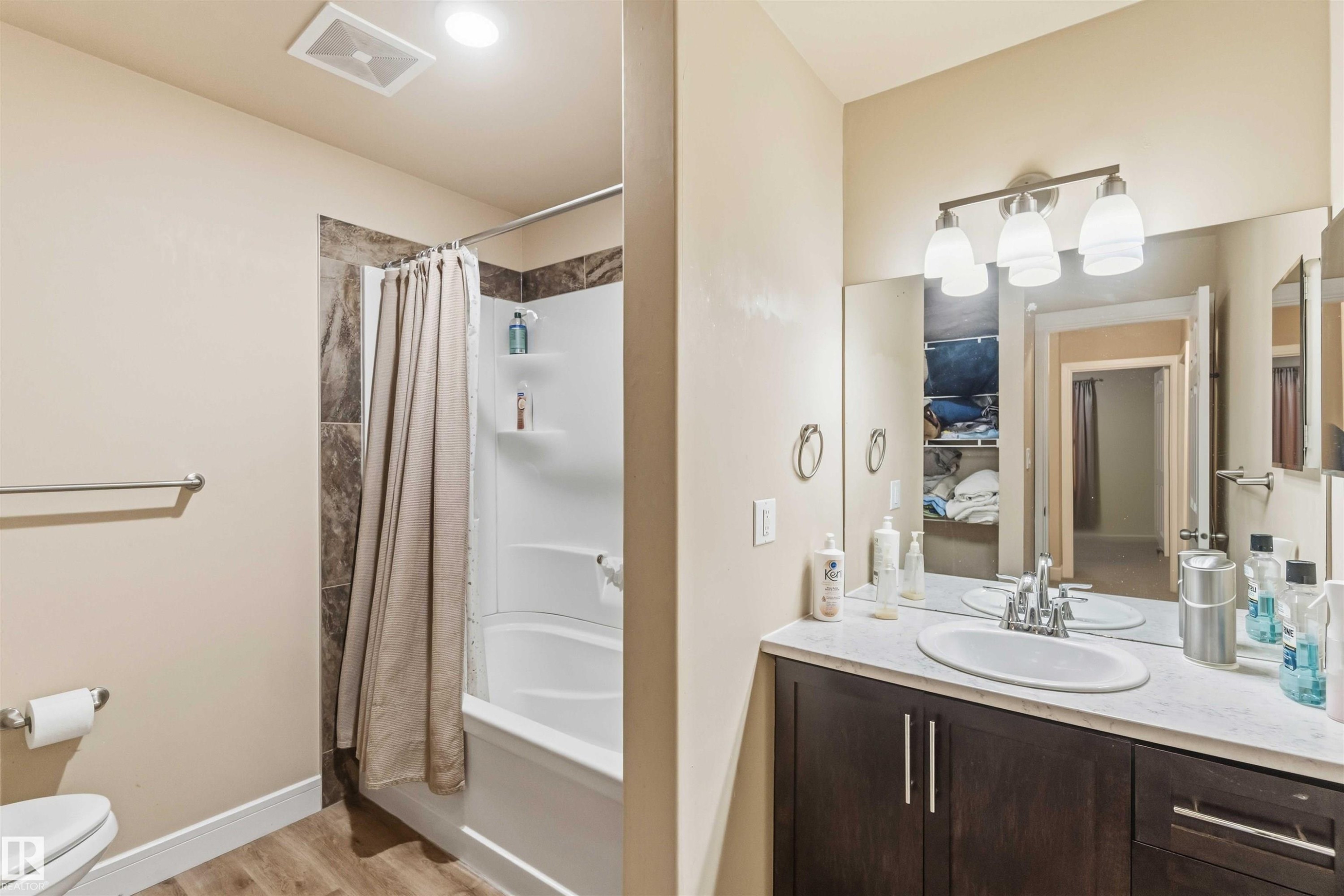 Bathroom featuring a shower-tub combination with tile surround, a single vanity with a dark wood-finish cabinet, and a large mirror - 17118 108 Street, Edmonton, AB