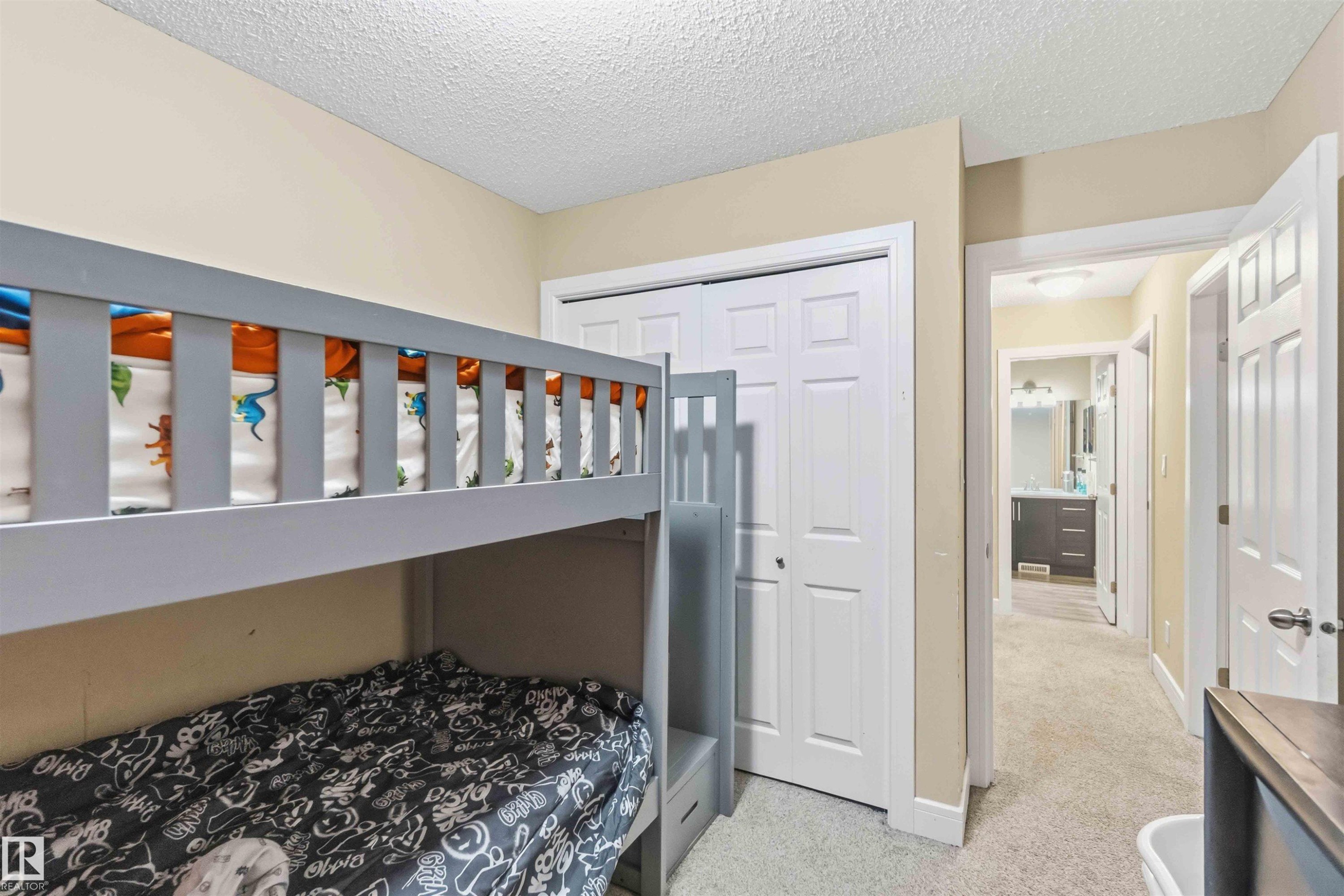 Bedroom featuring neutral wall paint, textured ceiling, light-toned carpet, and a white bi-fold closet - 17118 108 Street, Edmonton, AB