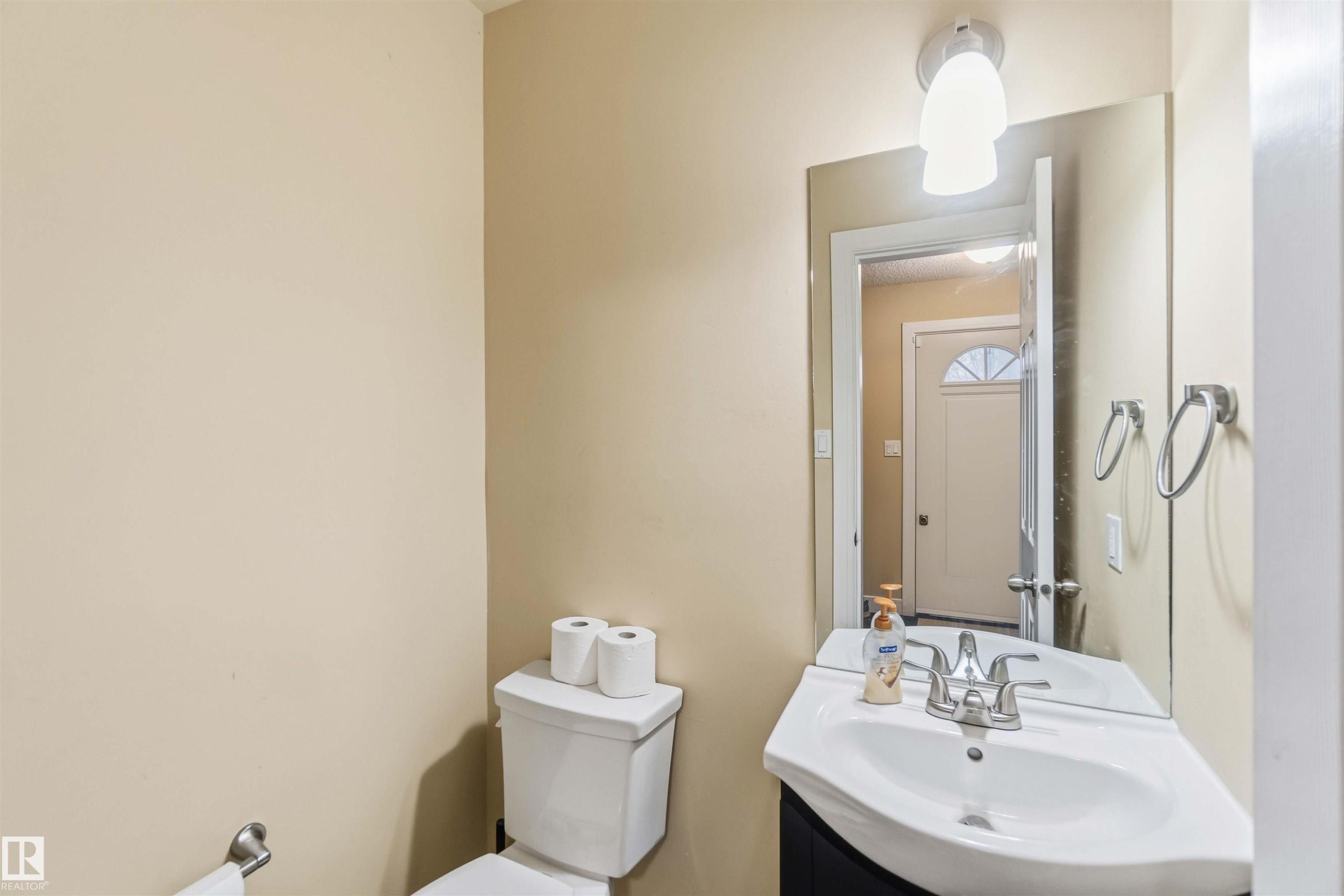 Compact powder room with a corner sink vanity, wall-mounted mirror, and overhead lighting fixture - 17118 108 Street, Edmonton, AB