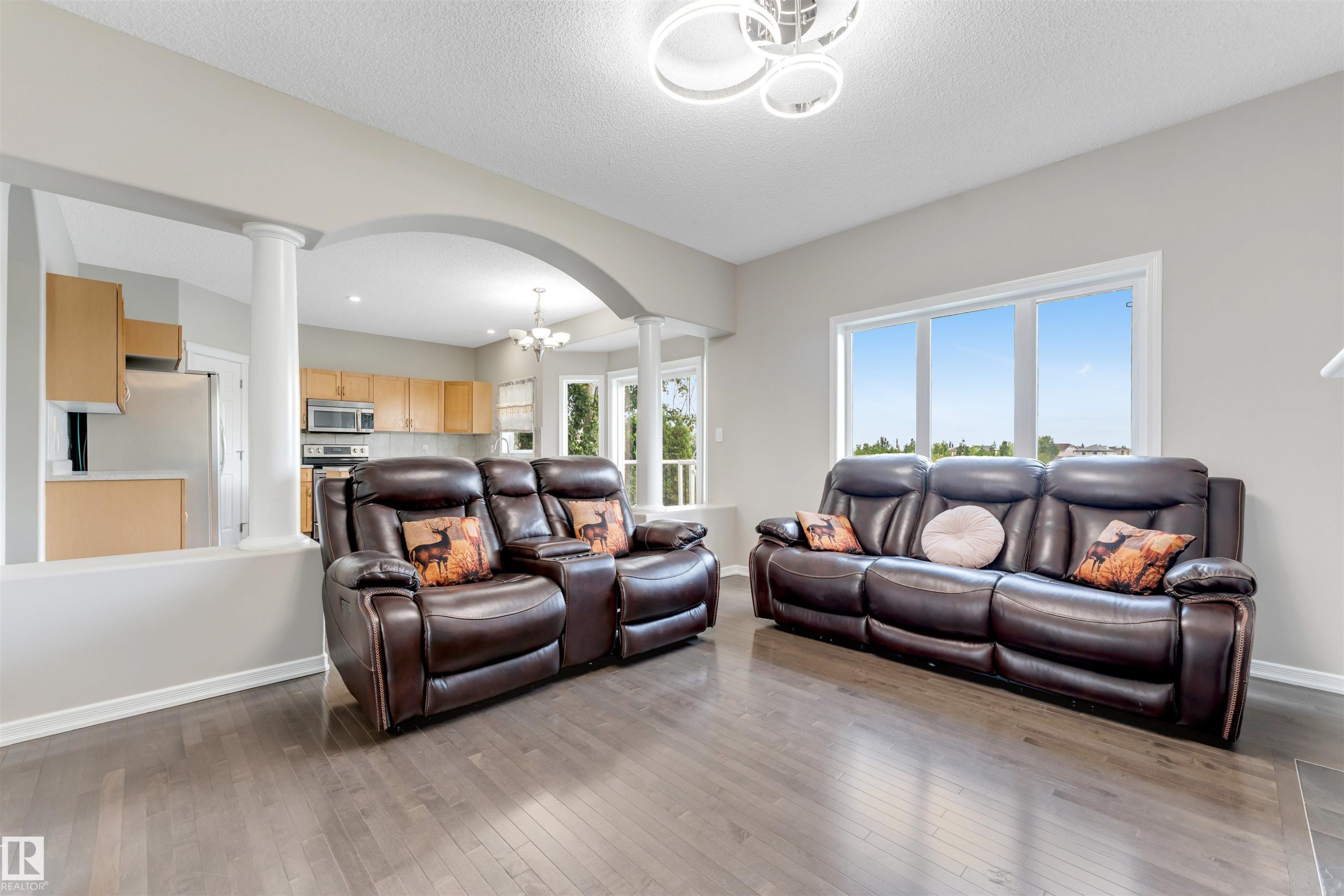 Spacious living area featuring wood-finish flooring, large windows, and a contemporary ceiling fixture - 3449 28 Street, Edmonton, AB