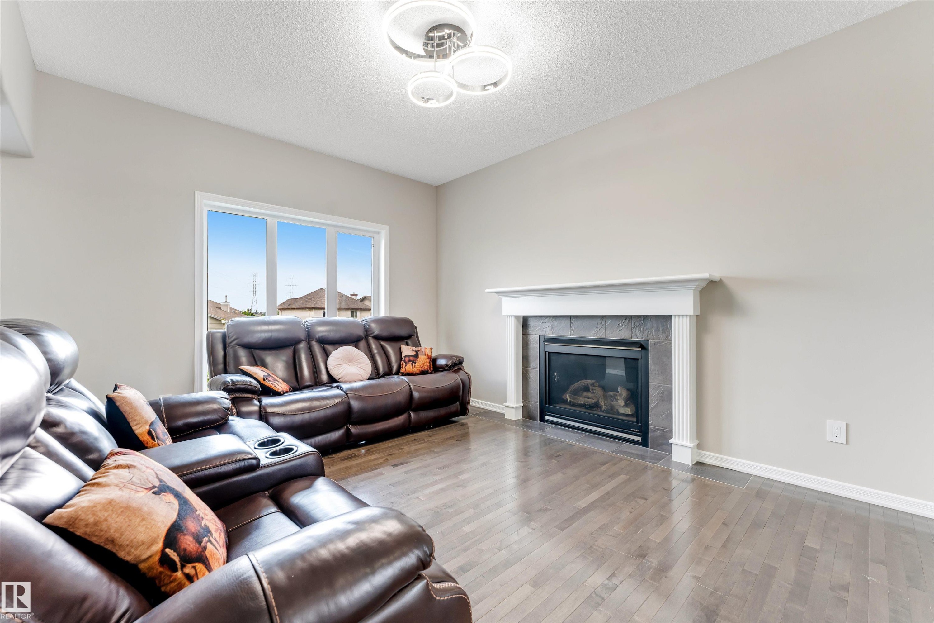 Living area featuring wood-finish flooring, a contemporary ceiling light fixture, and large windows - 3449 28 Street, Edmonton, AB