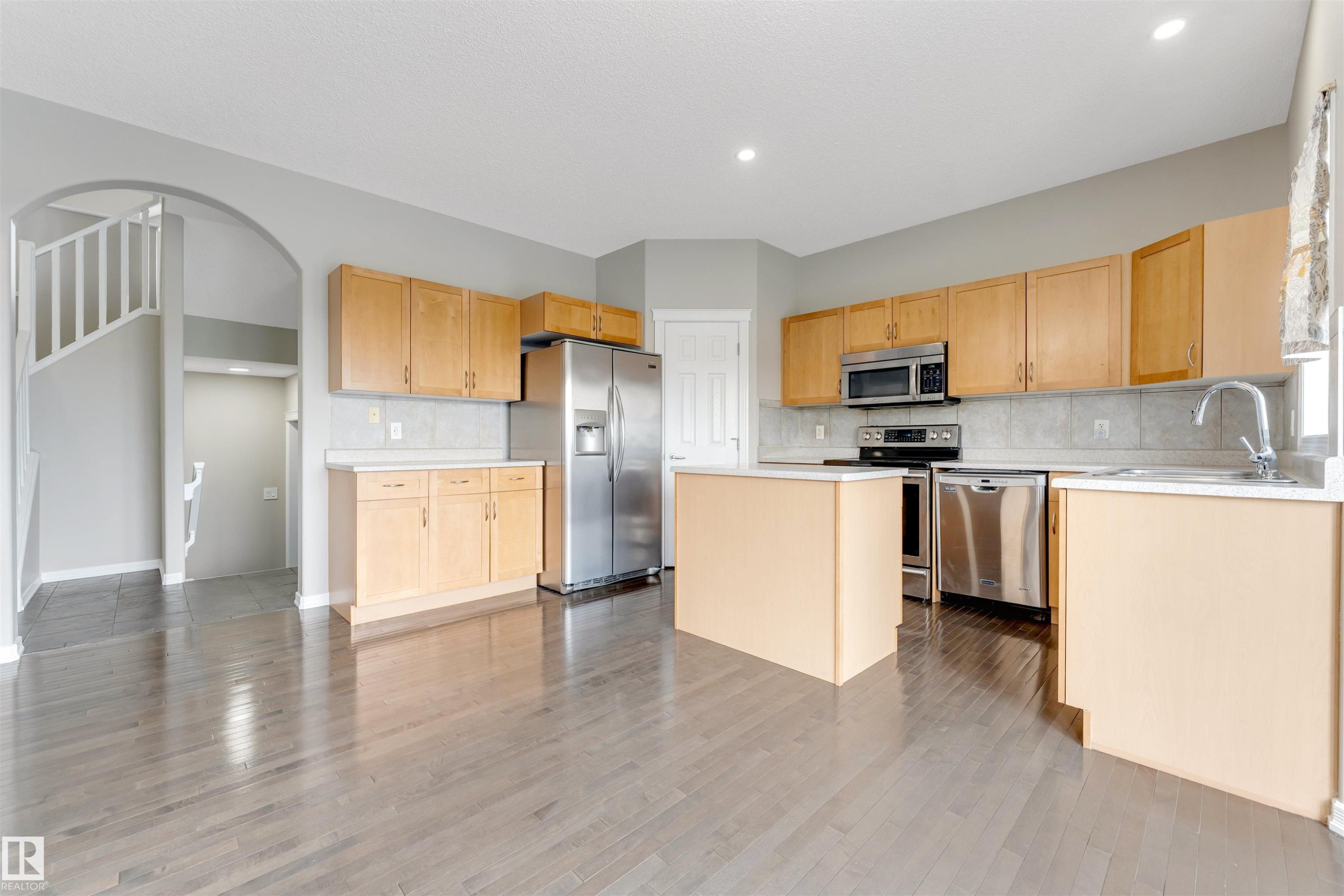 Kitchen featuring light wood cabinetry, stainless steel appliances, a center island, light-colored countertops, and tile backsplash - 3449 28 Street, Edmonton, AB