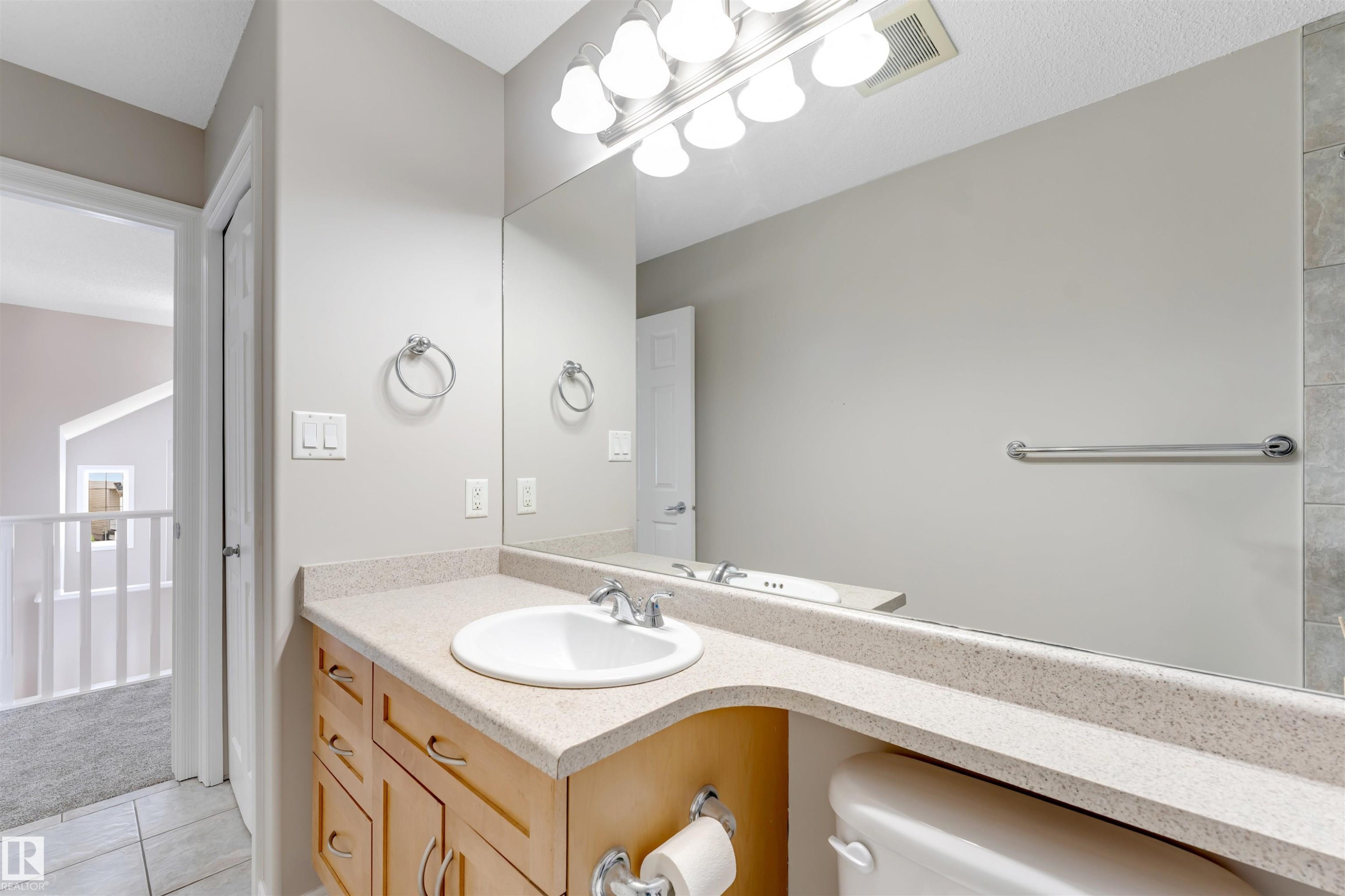 Bathroom vanity featuring a light-toned countertop with an integrated sink, polished chrome faucet, and expansive wall-mounted mirror - 3449 28 Street, Edmonton, AB