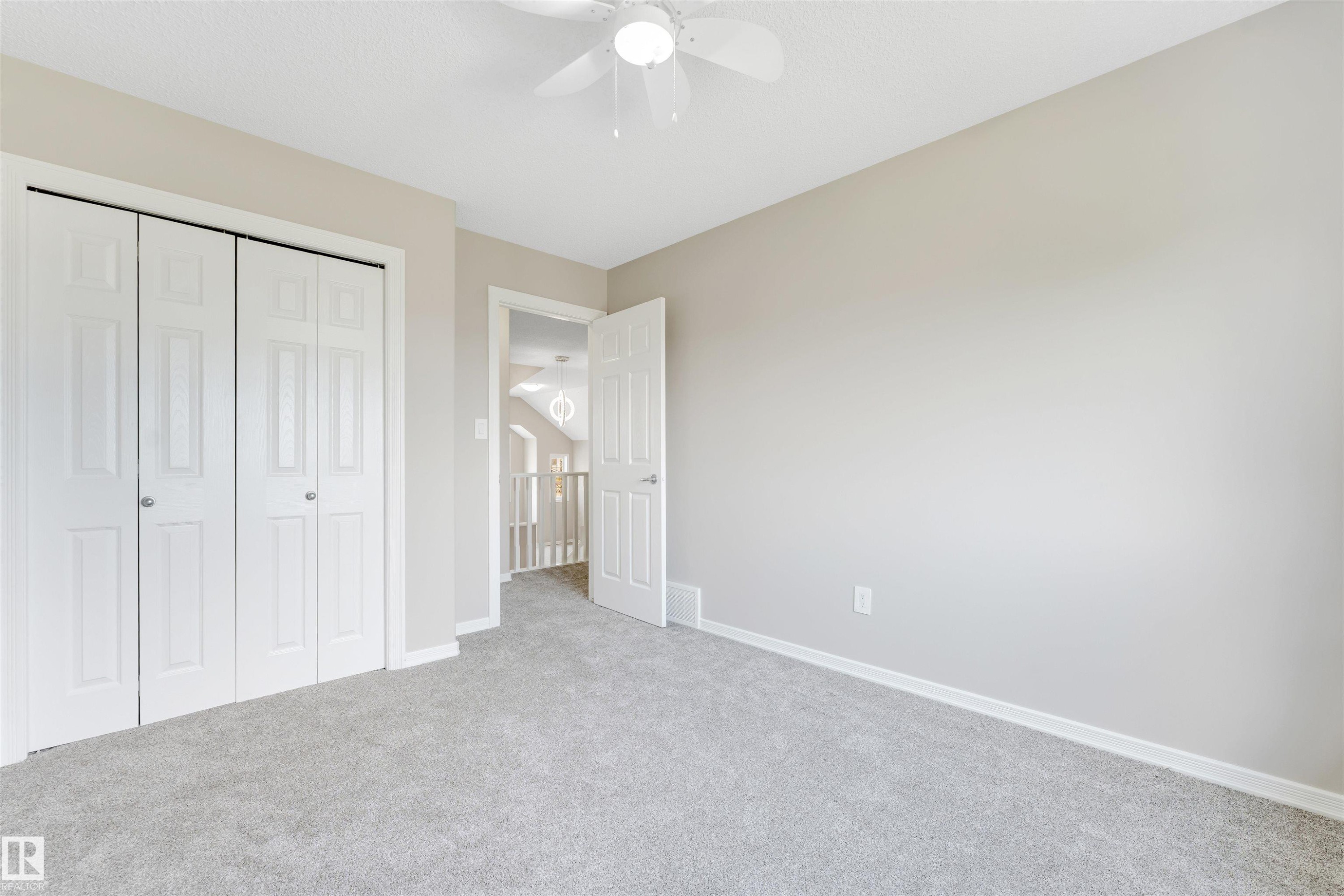 Neutral-toned room featuring a white ceiling fan, light gray carpet, and white bi-fold closet doors - 3449 28 Street, Edmonton, AB