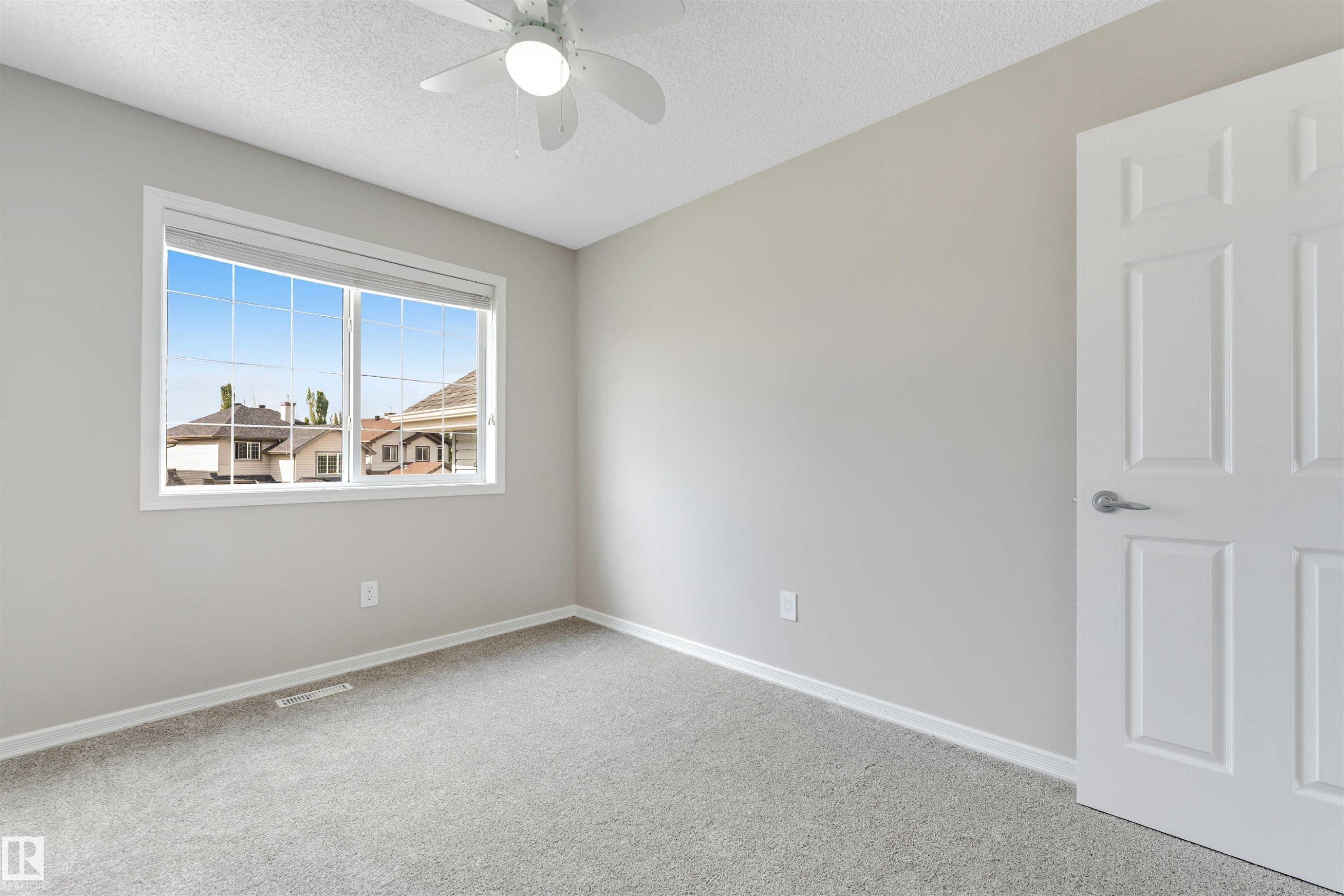 Neutral-toned room featuring a large window, light gray carpeting, and a white ceiling fan - 3449 28 Street, Edmonton, AB