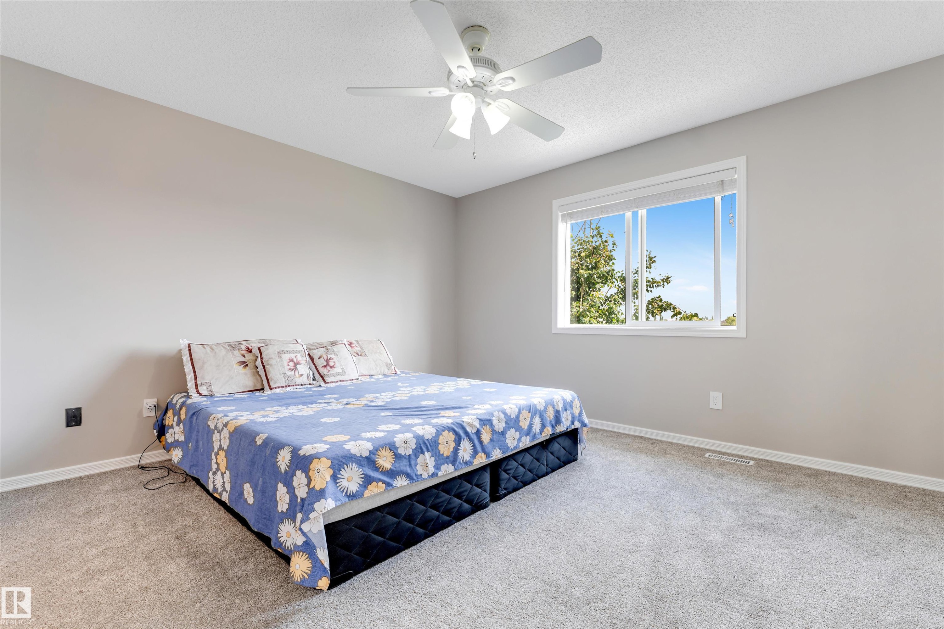 Carpeted room featuring a ceiling fan with integrated lighting, a large window with white trim, and light gray wall finishes - 3449 28 Street, Edmonton, AB