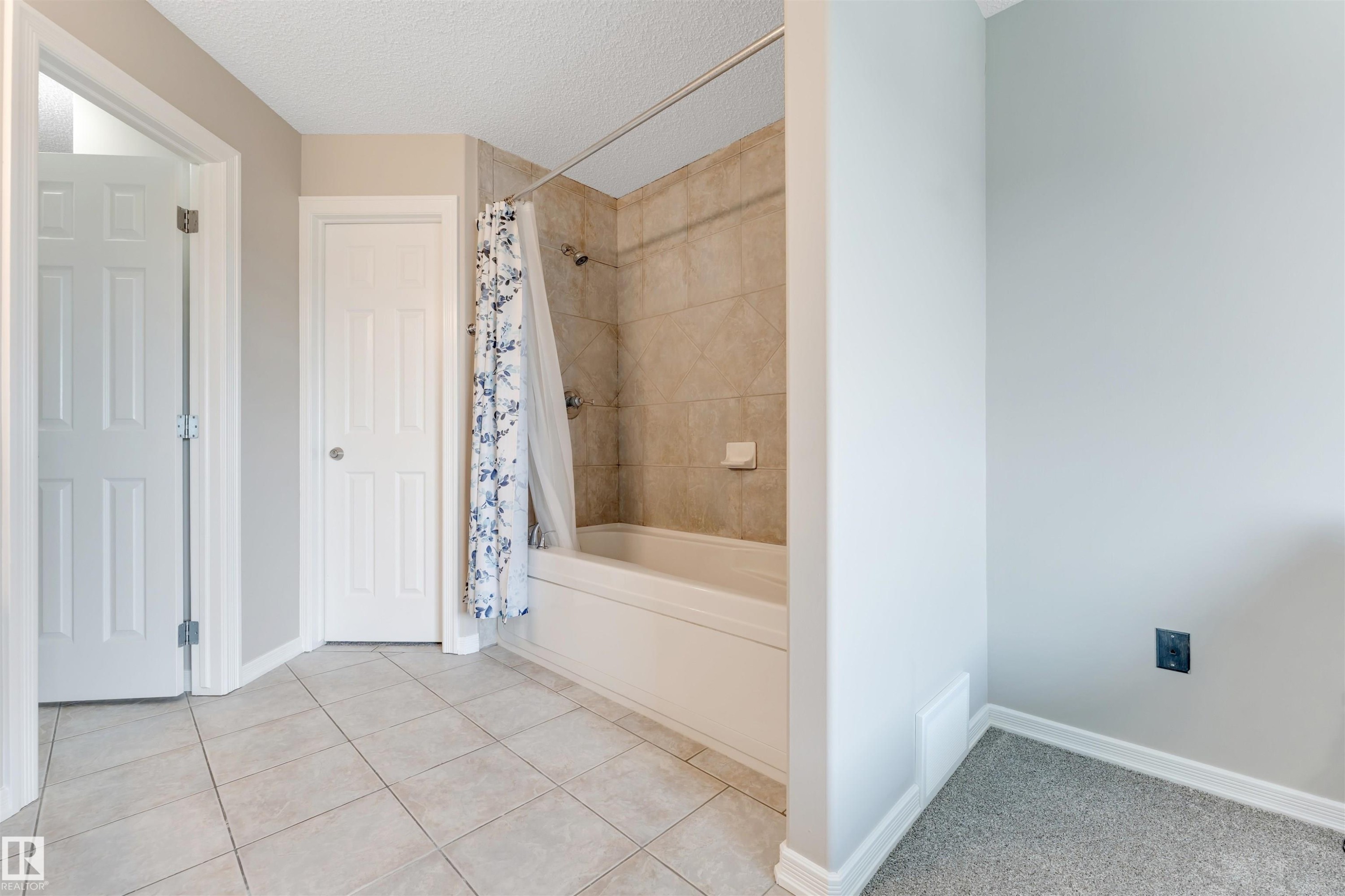 Bathroom featuring a tiled tub/shower combination with a shower rod, beige wall tiles, and a white tub basin - 3449 28 Street, Edmonton, AB