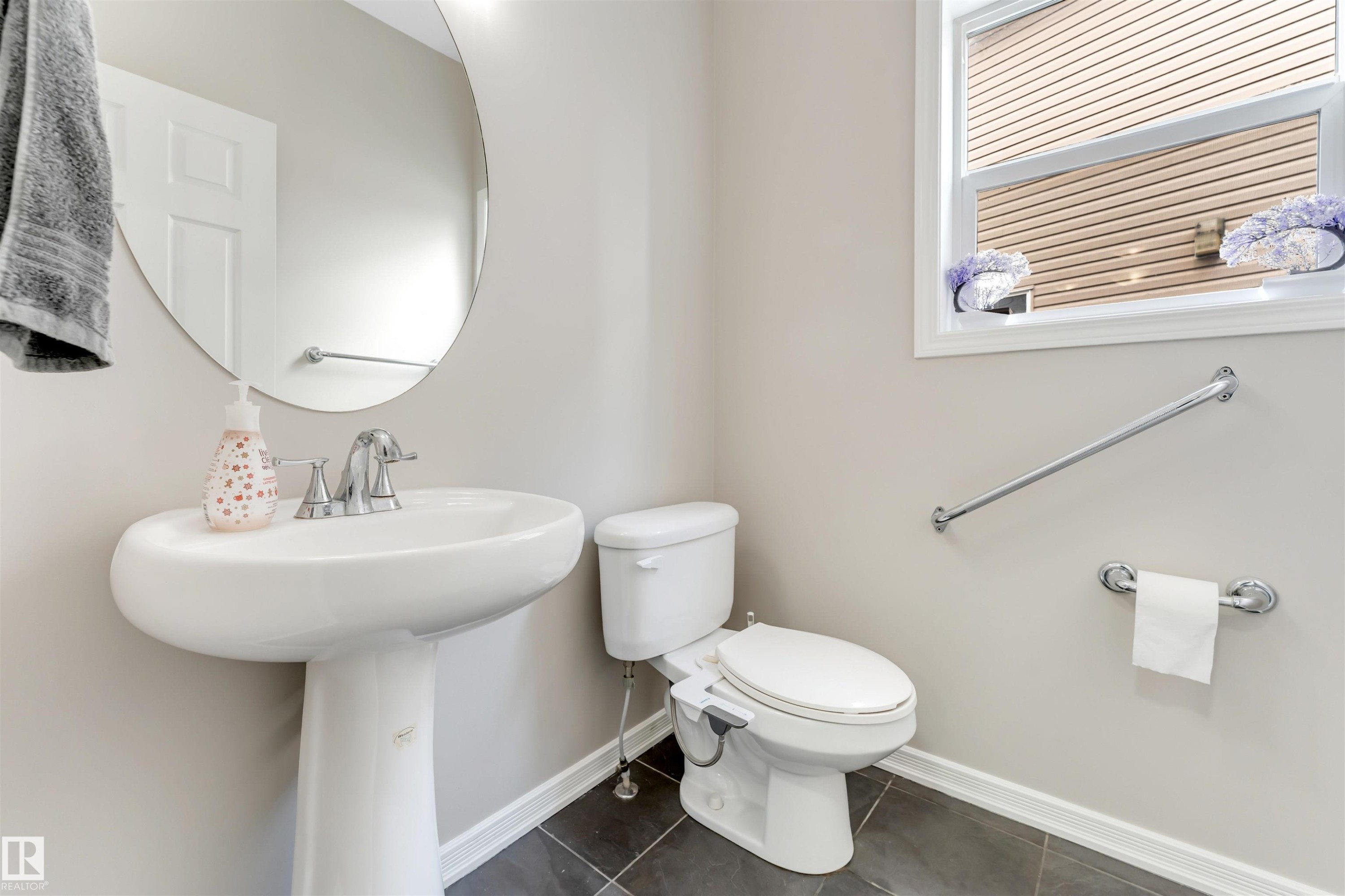 Pedestal sink with chrome faucet, circular mirror, and window with blinds - 3449 28 Street, Edmonton, AB