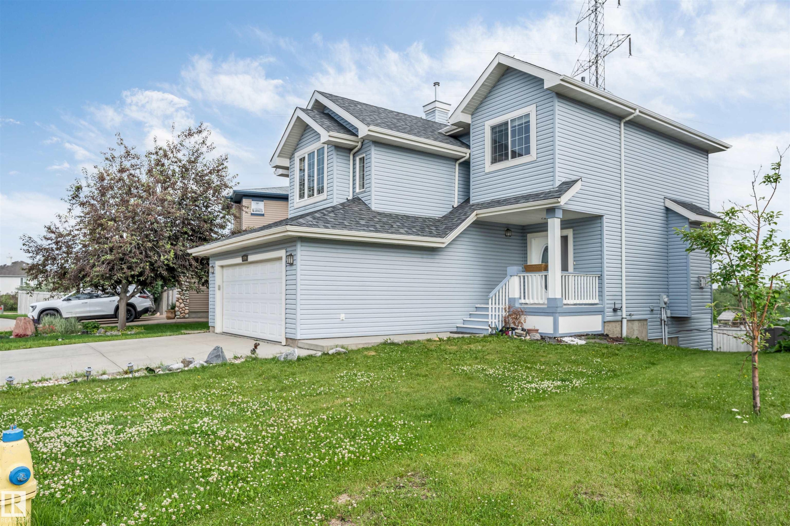 Two-story residence featuring light blue siding, an attached garage, a covered front entry, a concrete driveway, and a sloped lawn - 3449 28 Street, Edmonton, AB