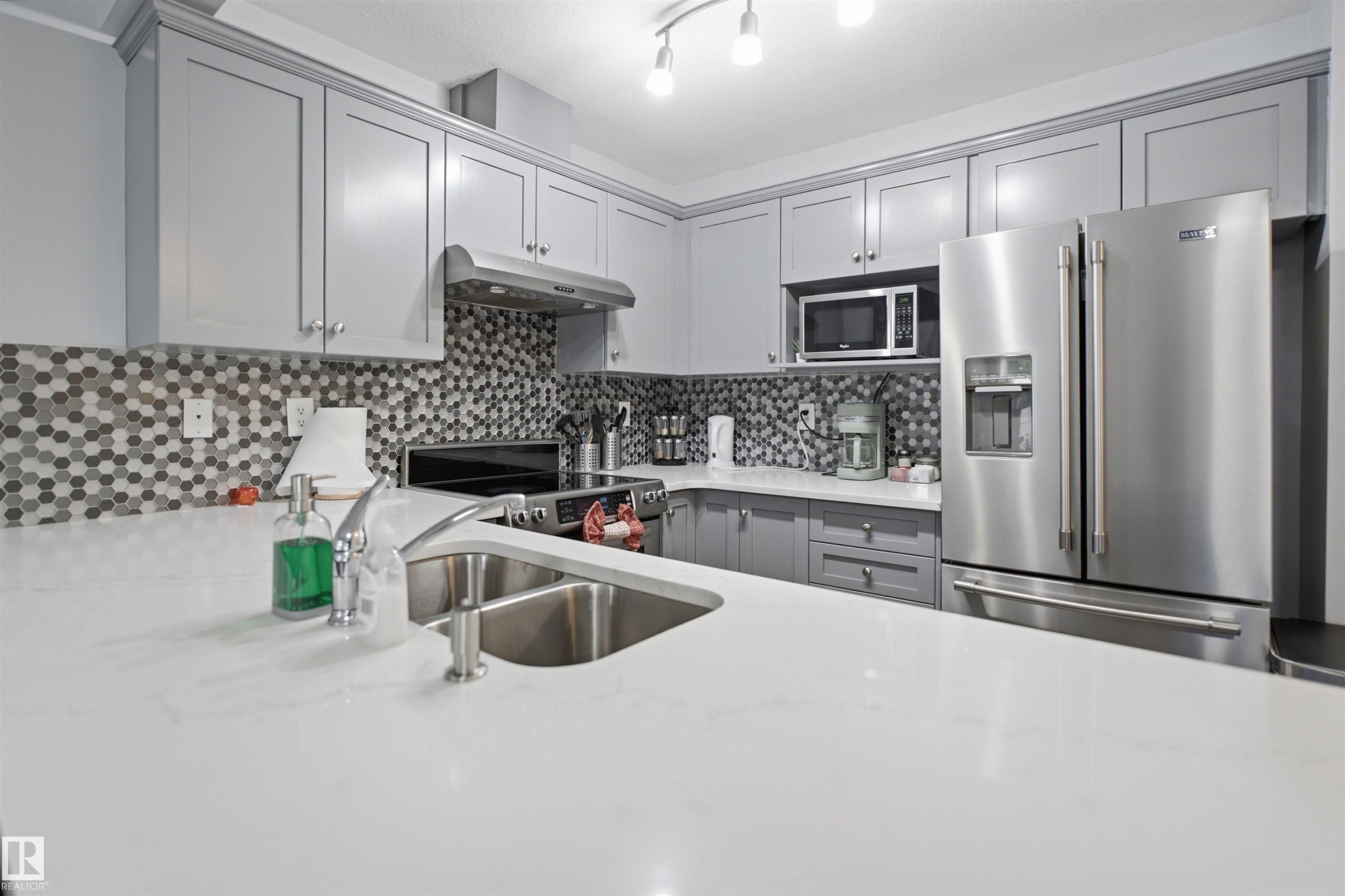Kitchen featuring white countertops, grey shaker-style cabinetry, and a mosaic tile backsplash - 92 230 Edwards Drive, Edmonton, AB