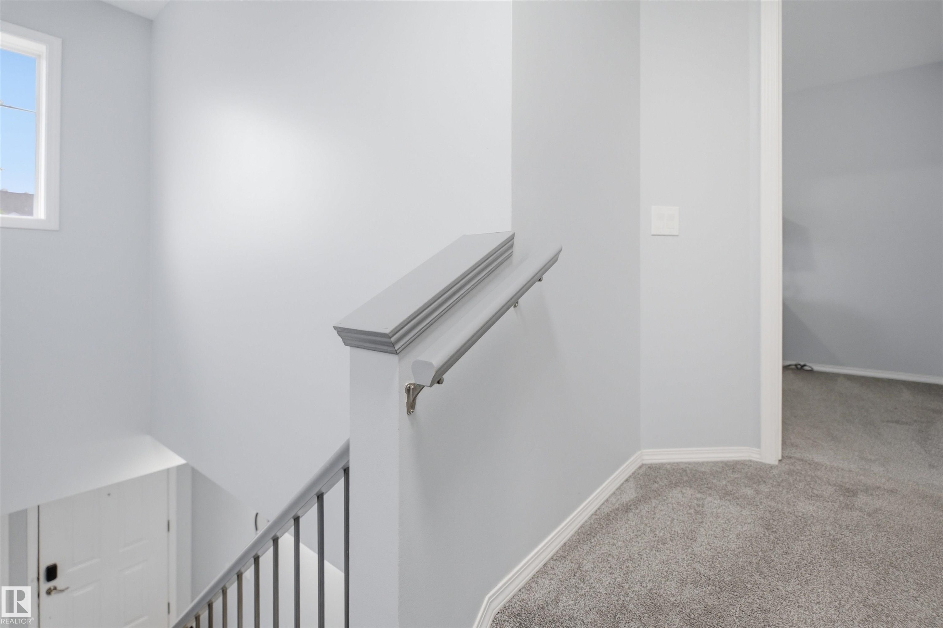 Staircase featuring painted wooden newel post, metal balusters, and a light gray handrail - 92 230 Edwards Drive, Edmonton, AB